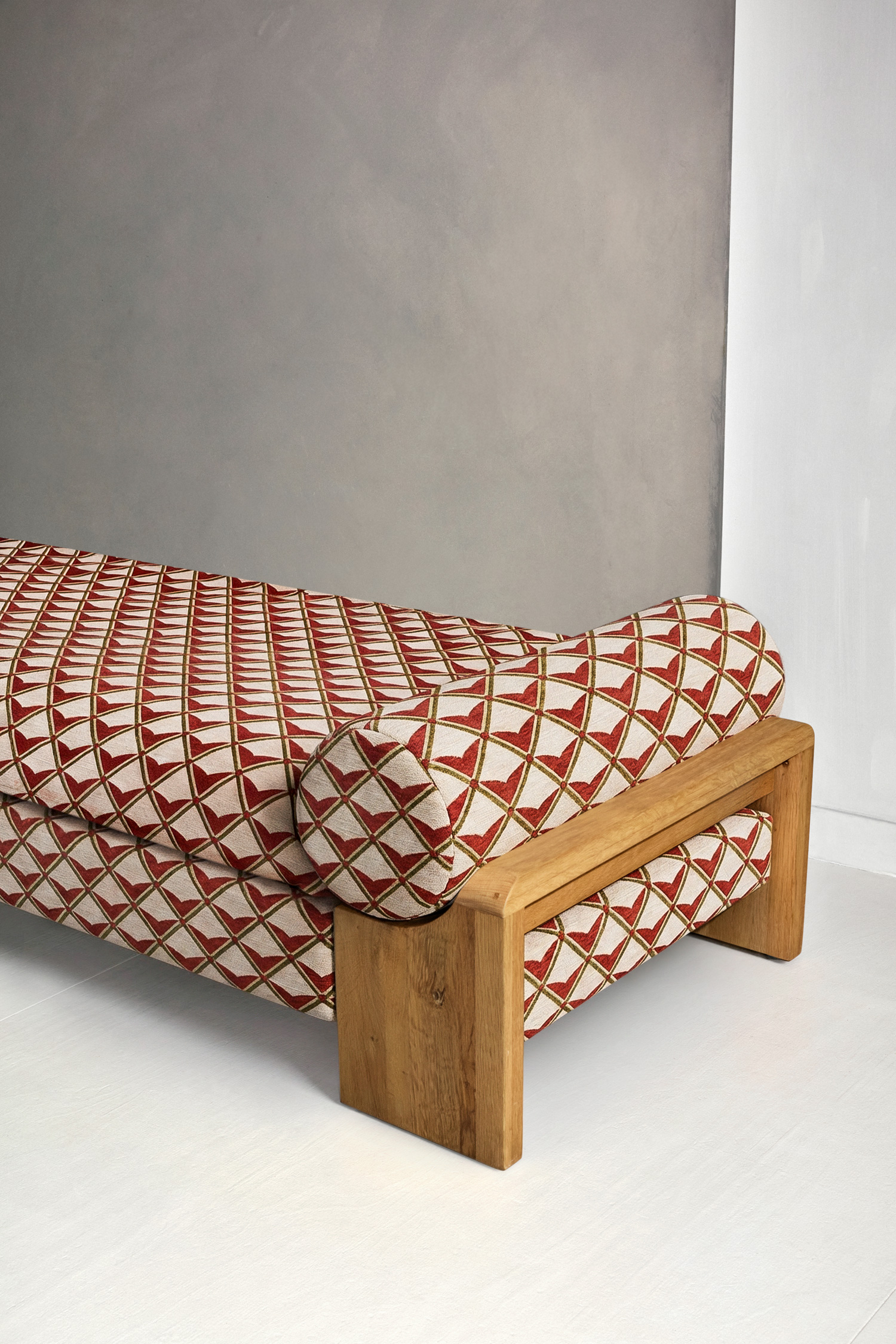 A wooden bench with a patterned cushion and a matching pillow, placed against a plain wall with a white baseboard.