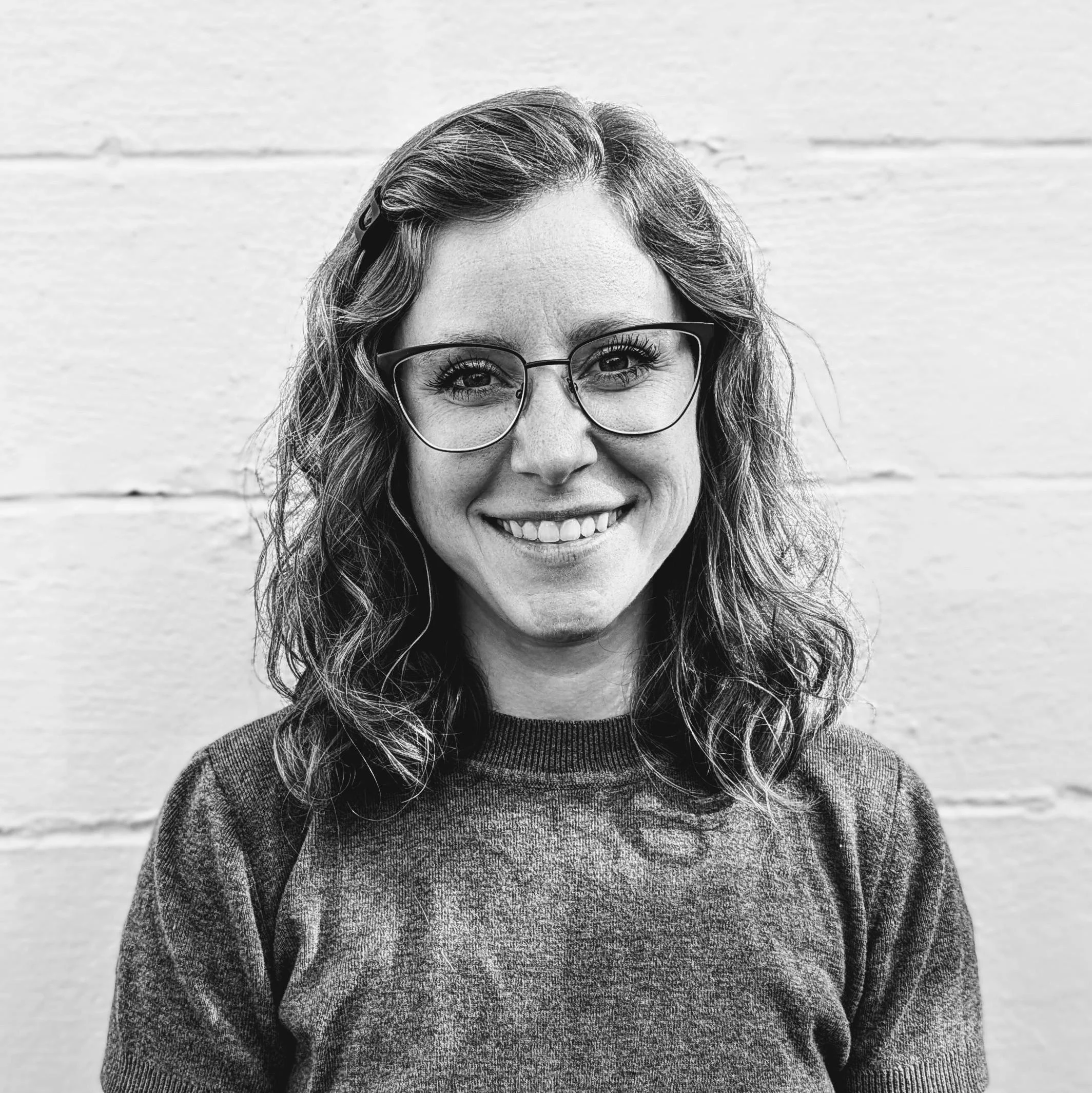 A black and white photograph of Hayley Whitaker, Nursery Coordinator, smiling in front of a white wall.