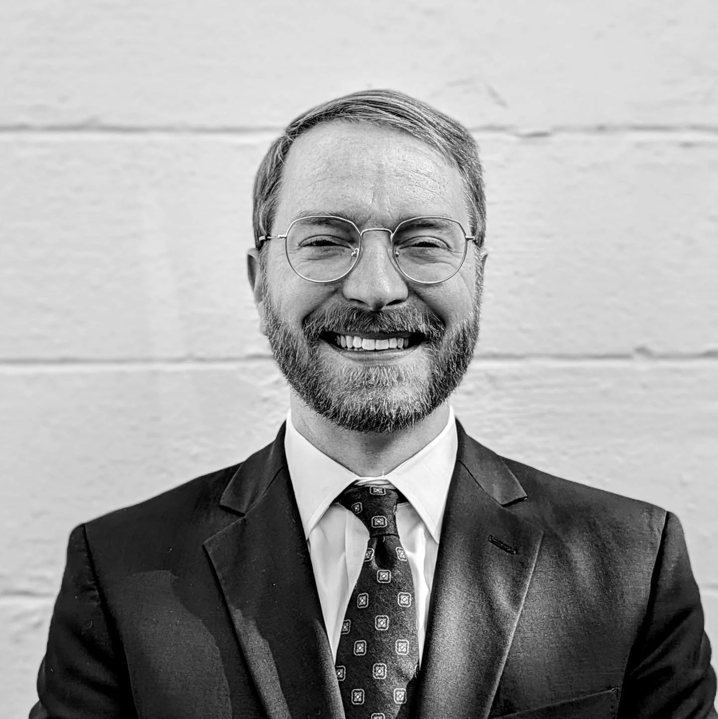 A black and white photograph of Pastor Jason Piland smiling in front of a white wall.