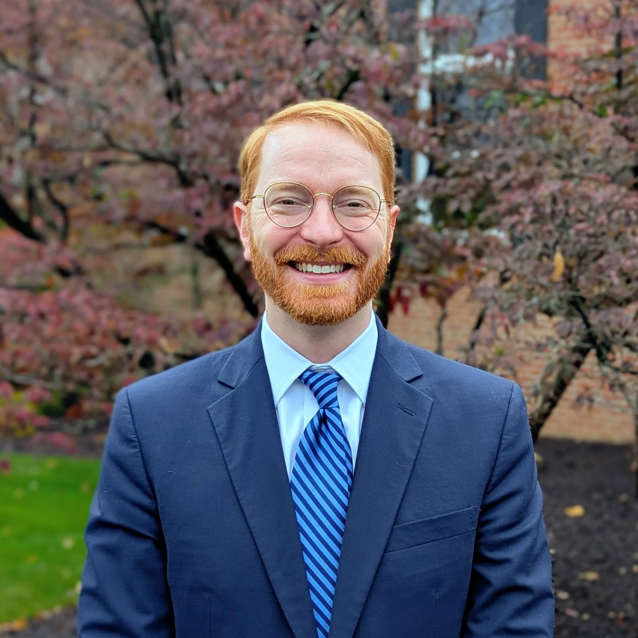 Headshot of Pastor Piland in wire glasses wearing a navy jacket and blue striped tie.