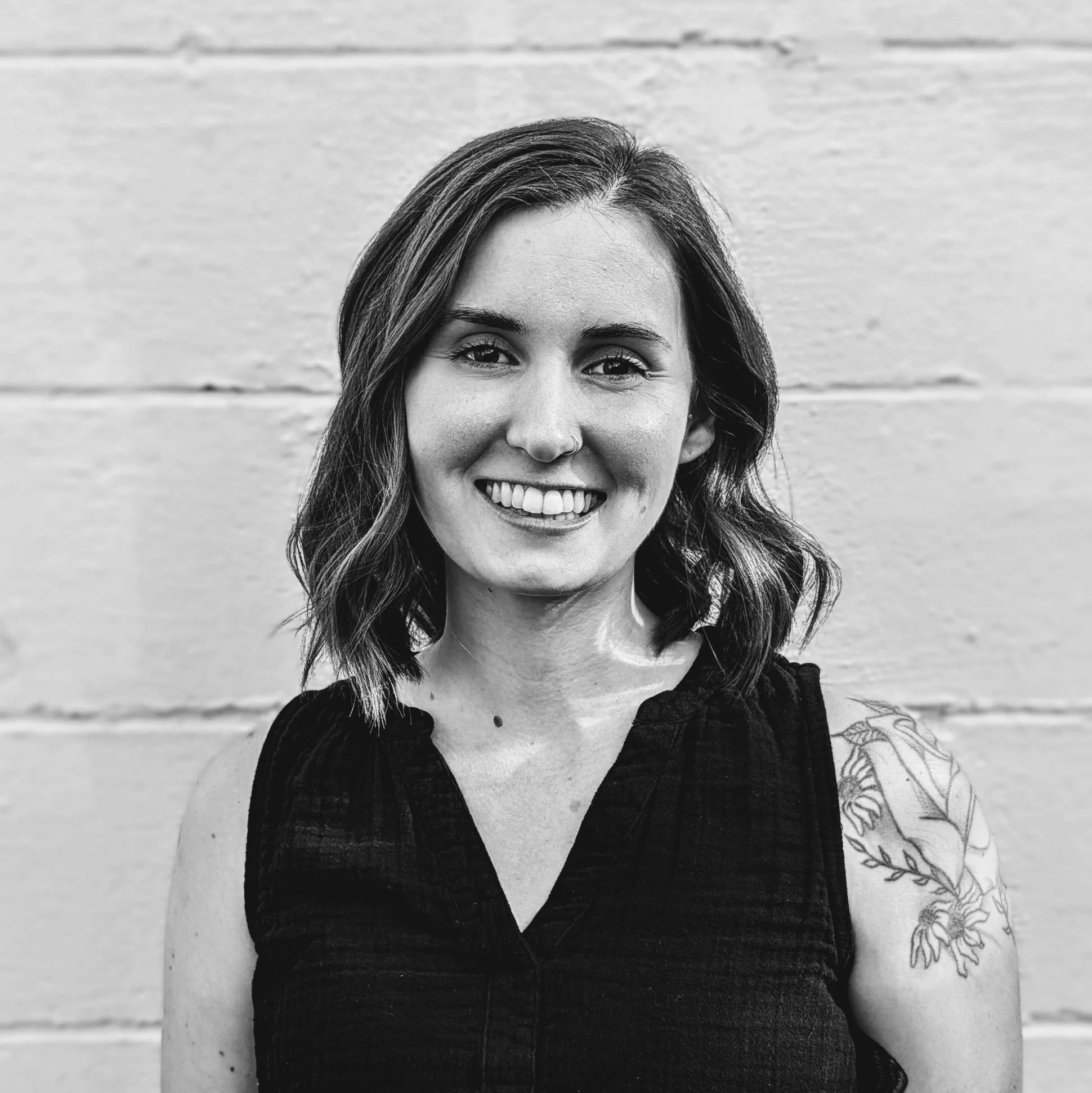 A black and white photograph of Michala Halterman, Administrative and Communications Assistant, smiling in front of a white wall.