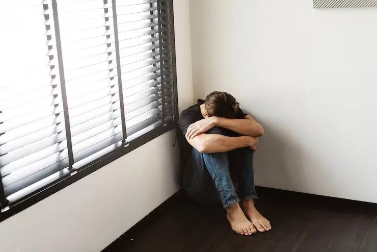 person-sitting-floor-head-down-near-window-with-blinds