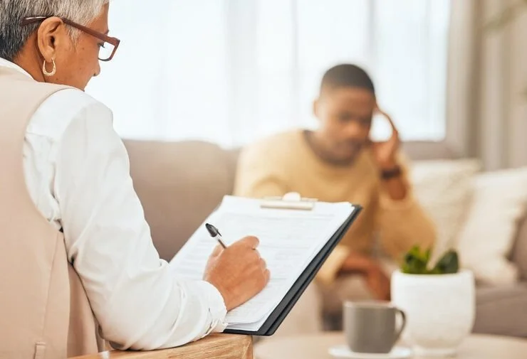A therapist taking notes during a therapy session with a patient talking on the phone in a cozy living room.