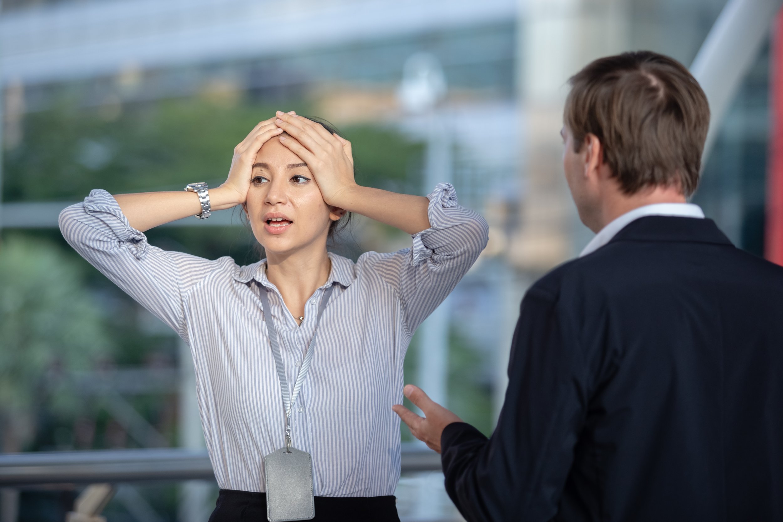 A woman appears distressed with her hands on her head, talking to a man in a suit, in an office or conference setting.