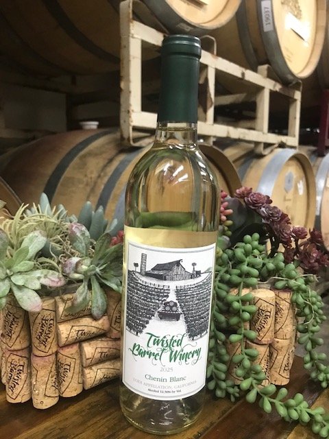 A bottle of white wine labeled 'Twisted Carrel Winery' with a vineyard and winery illustration, surrounded by grapevine and succulent plants, in a wine cellar with barrels in the background.