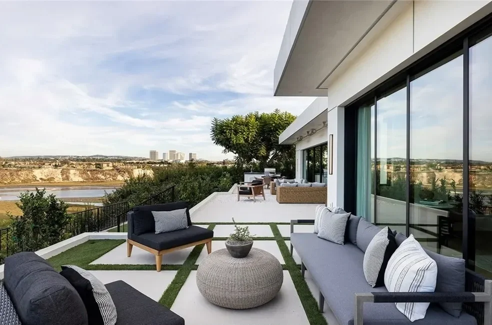 Modern balcony with gray seating, a round pouf, and a view of a canyon with buildings in the distance.
