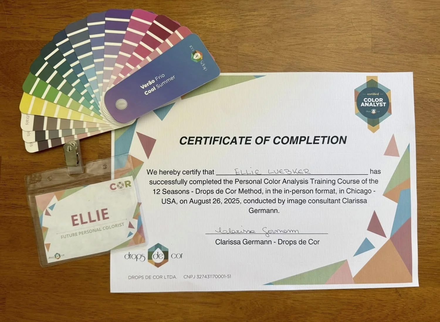 Certificate of completion for Ellie Luebker from a color analysis training course, a color palette fan, and a name badge with Ellie's name and colorful geometric pattern.