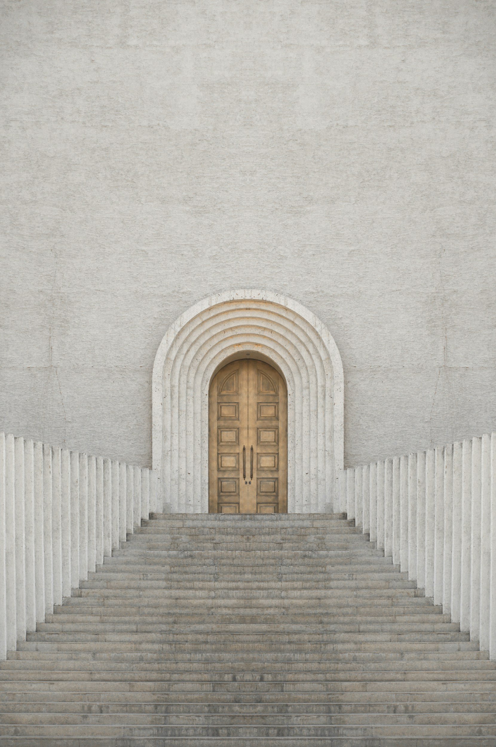 A symmetrical view of a stone staircase leading up to a wooden door set into a large white wall with an arch surrounding the door, flanked by off-white vertical ribbed columns.