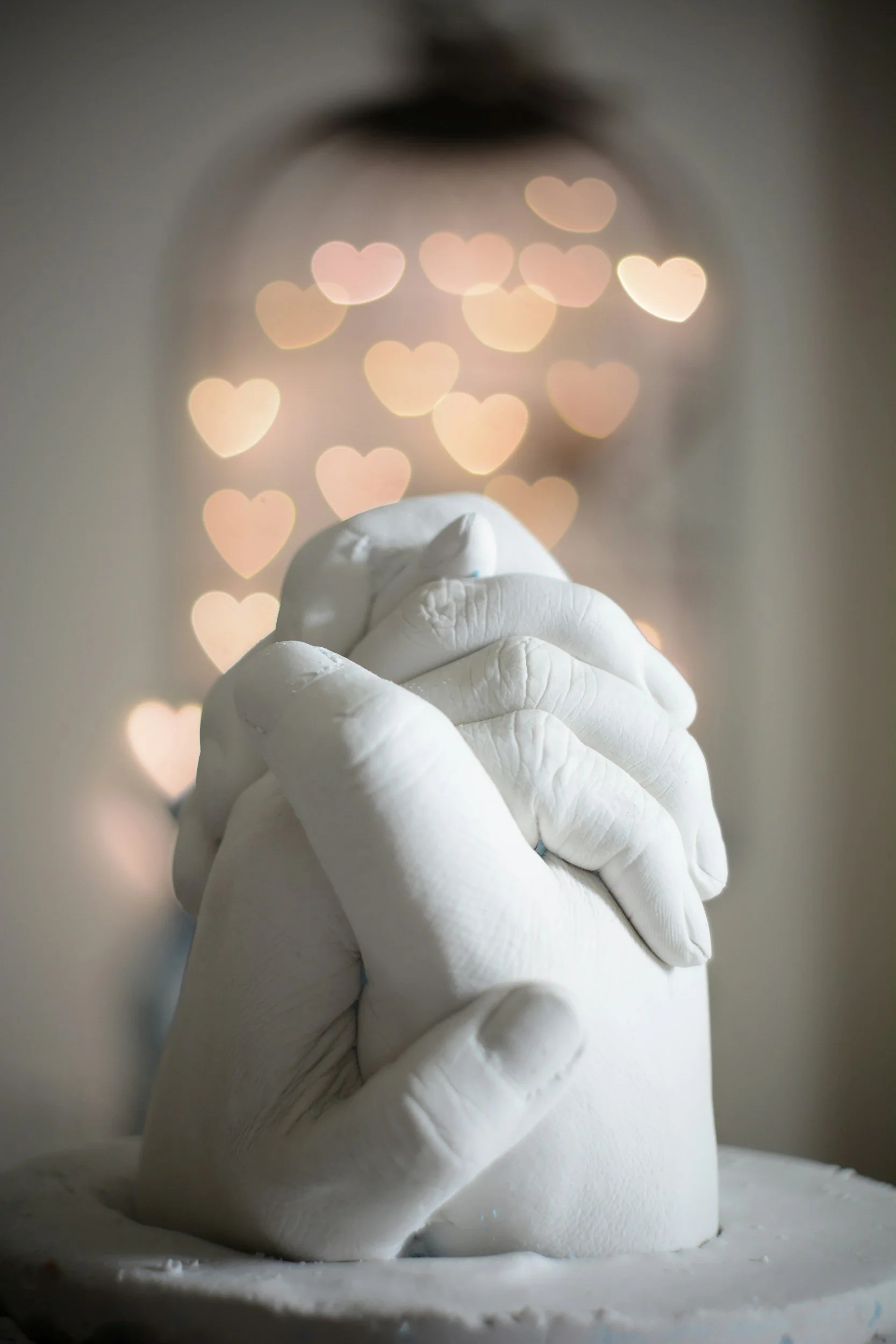 Close-up of a white wedding cake with a fondant hand holding a small cake topper, with blurred heart-shaped bokeh lights in the background.