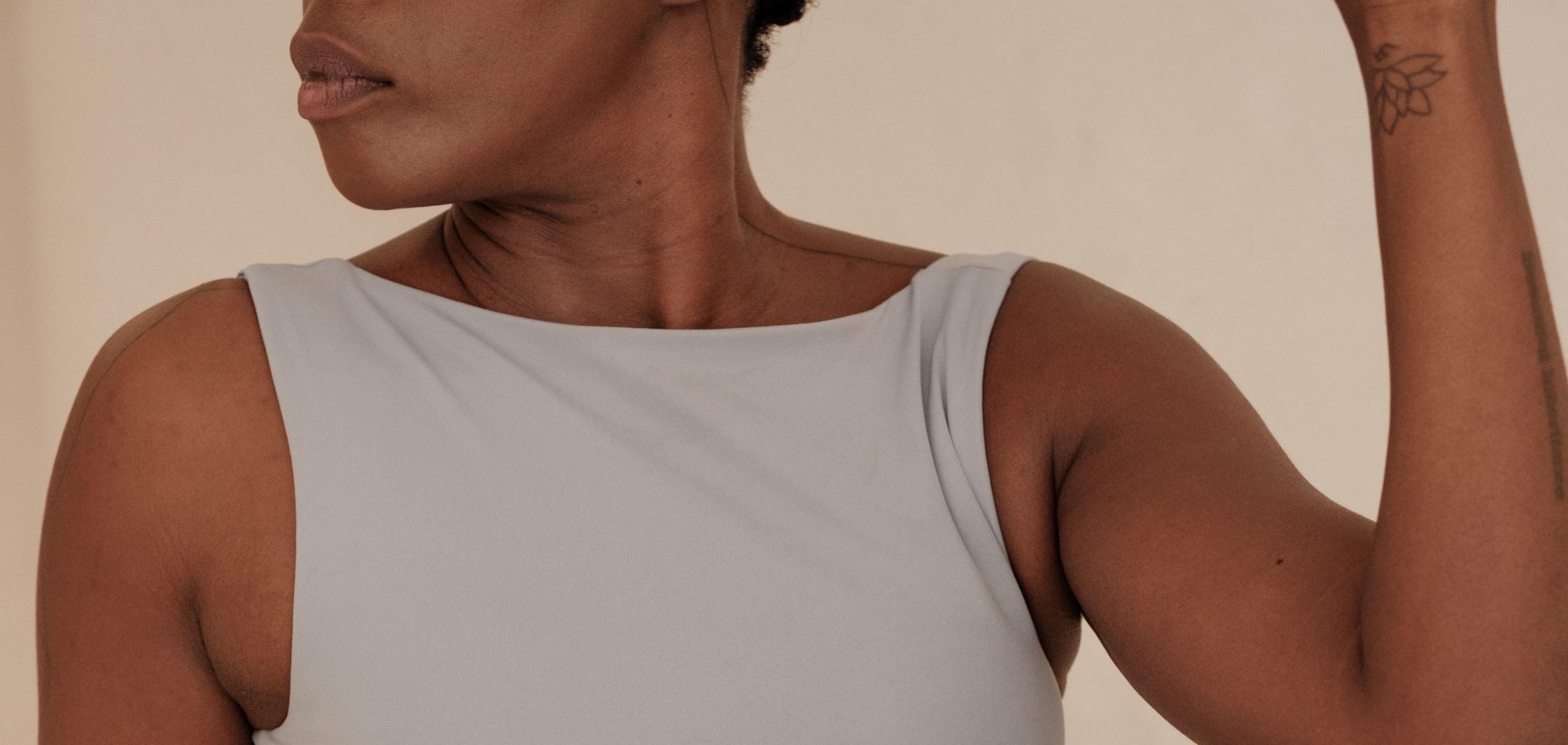 A woman wearing a sleeveless white top, showing her arm with a tattoo, her face turned away.