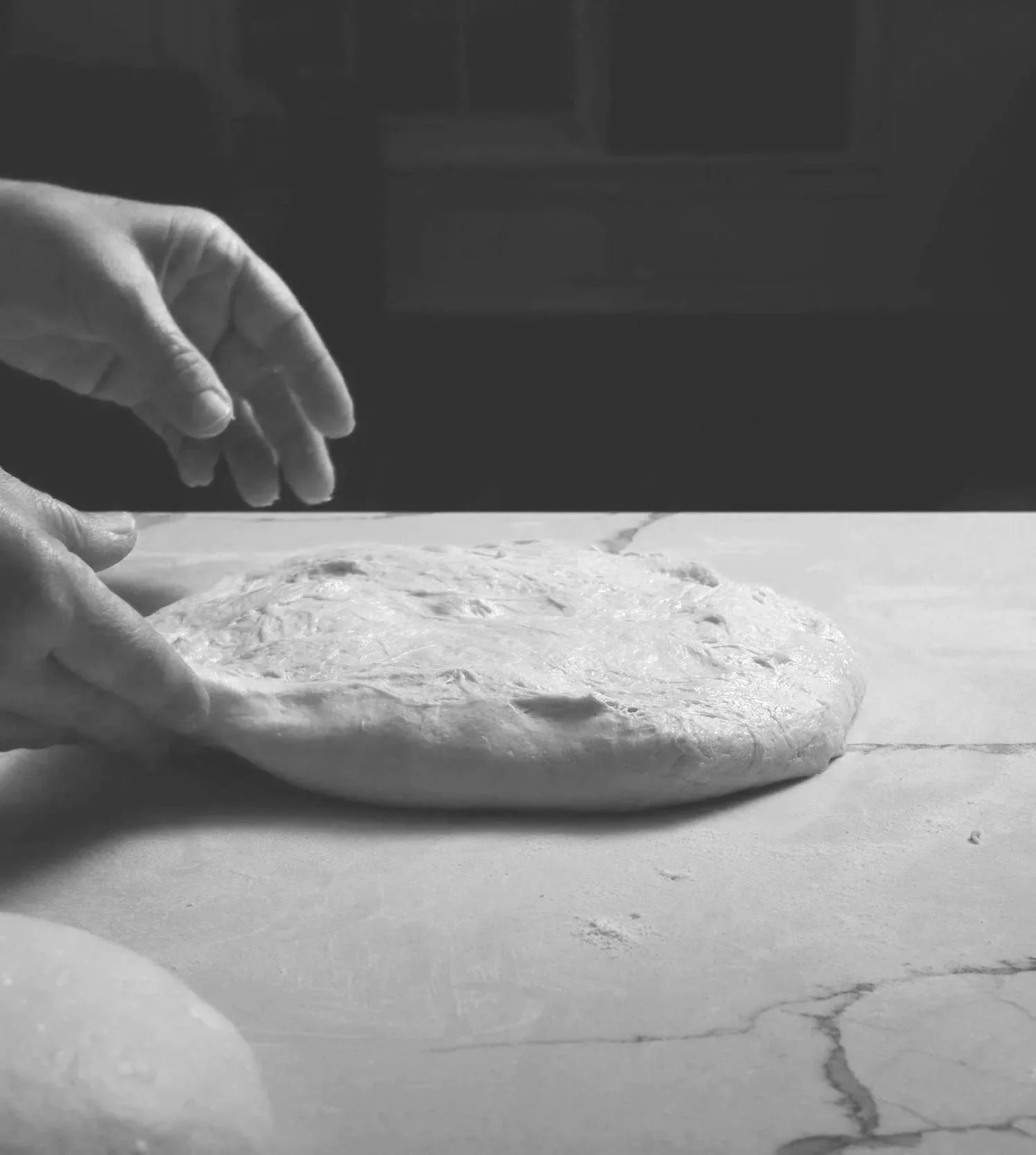A person is kneading sourdough on a kitchen countertop in black and white.