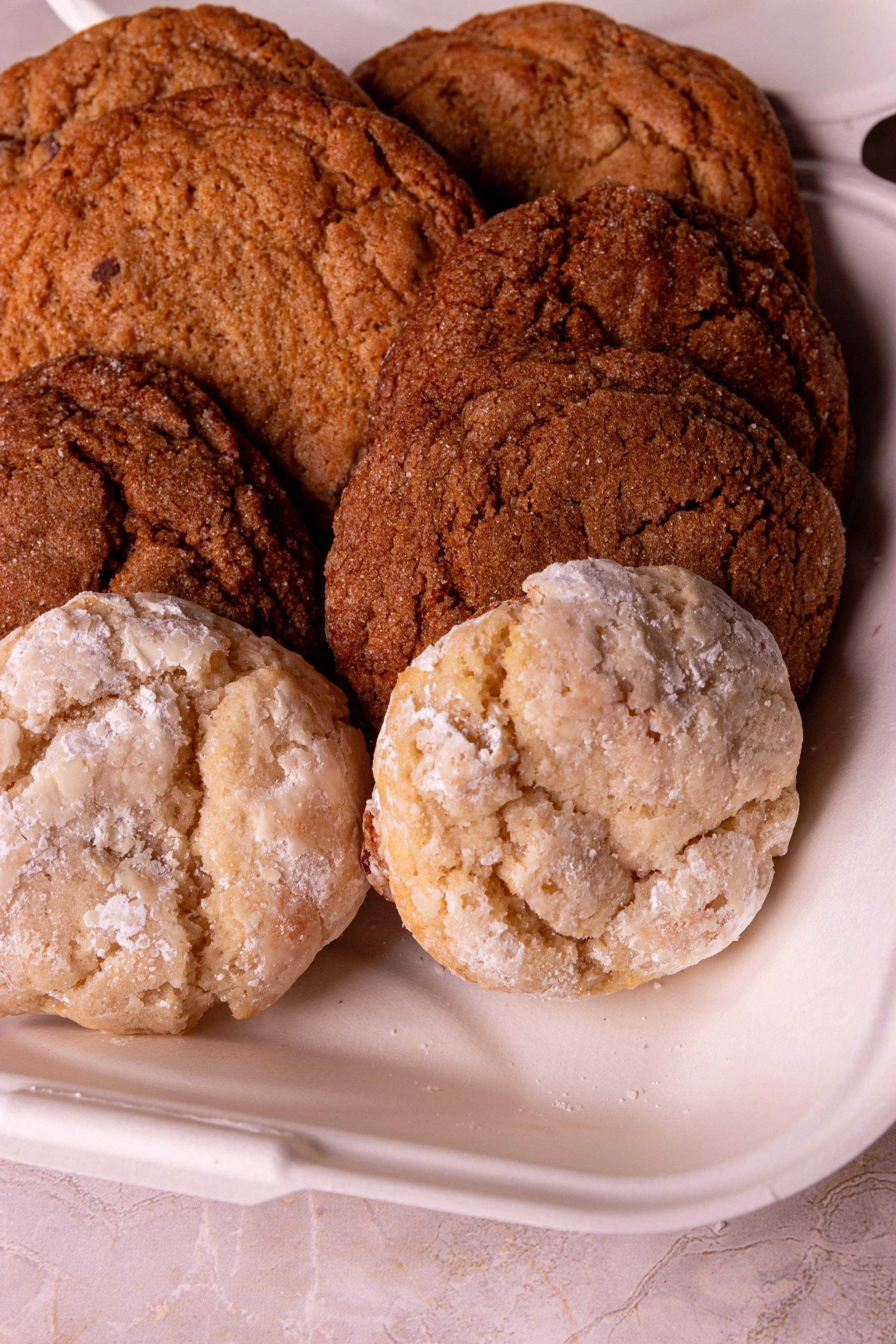 A close-up of assorted cookies, including ginger molasses, sugar, and chocolate chip cookies, arranged in a white container.