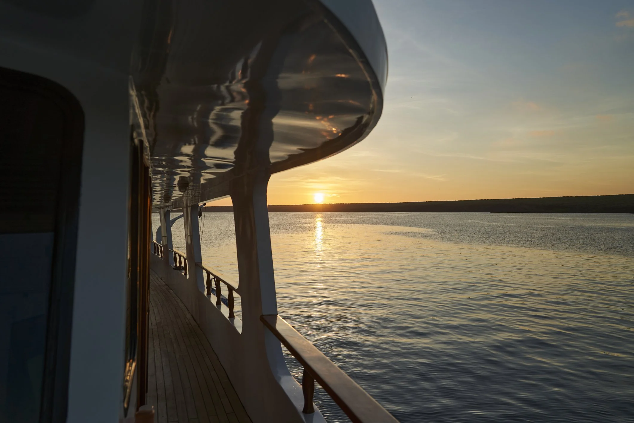 View from a boat deck during sunset with calm water and a distant shoreline.