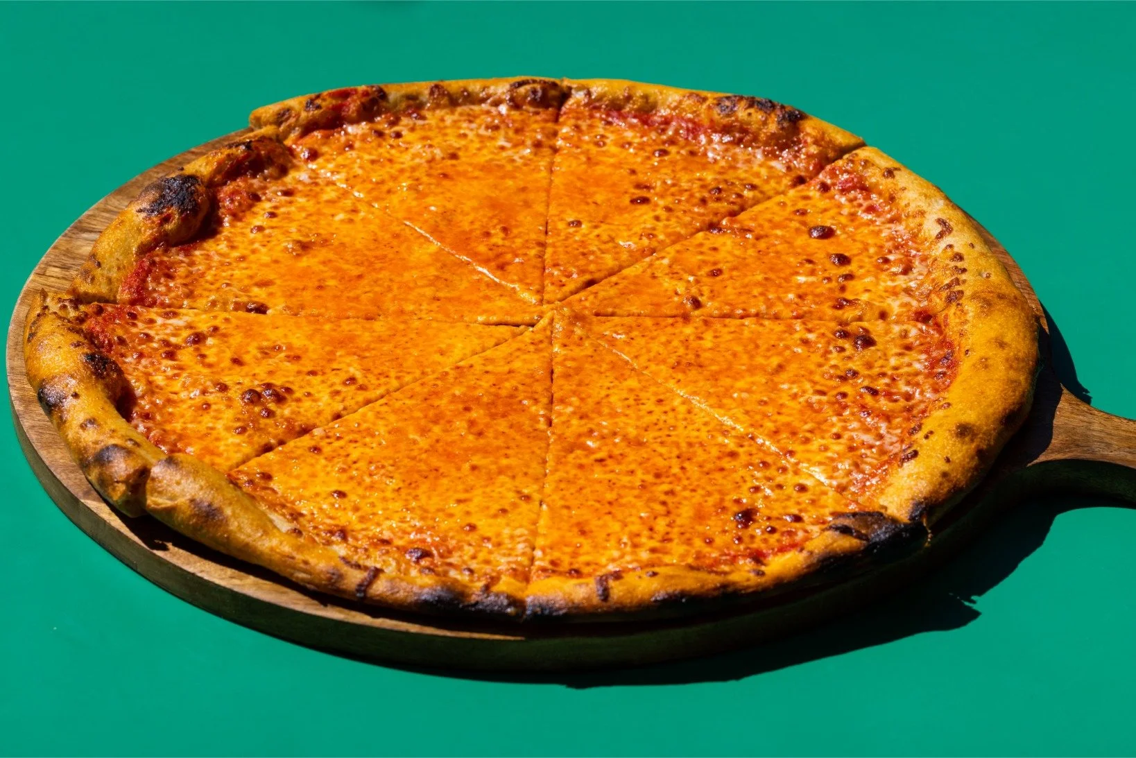 Cheeseburger pizza on a wooden serving board against a green background.