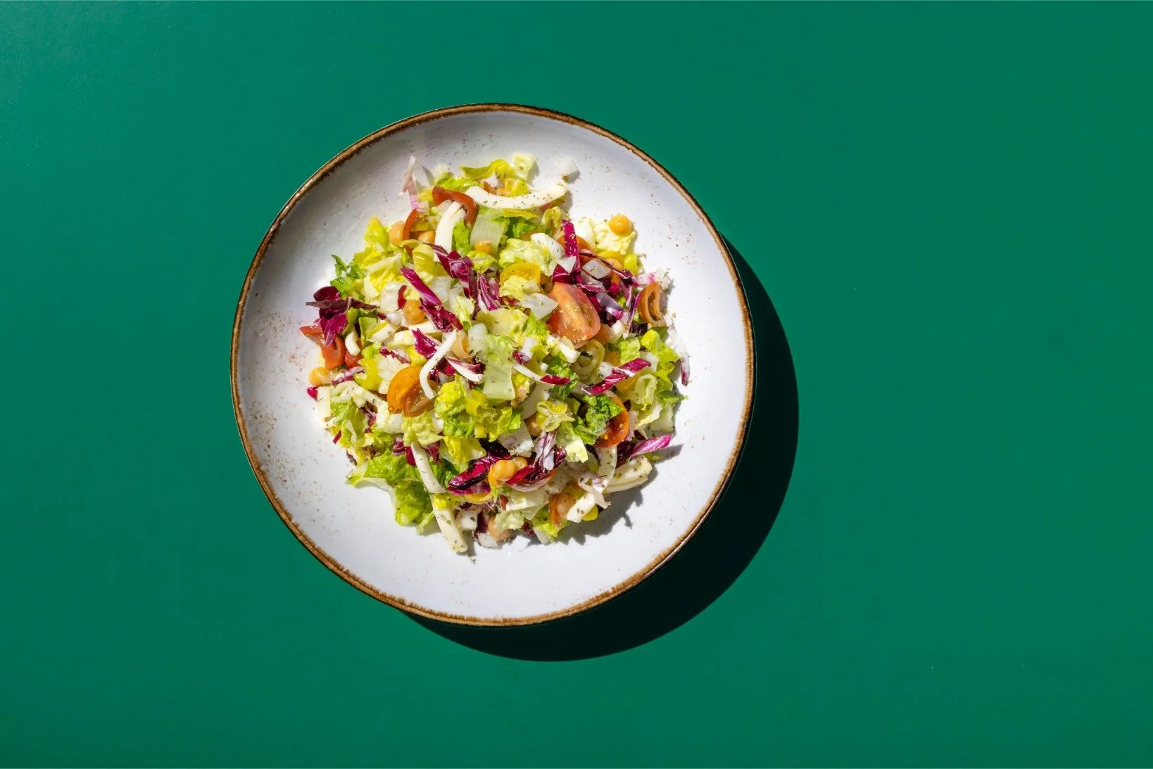 A white ceramic plate with a salad of chopped lettuce, purple cabbage, cherry tomatoes, and corn, on a green surface.