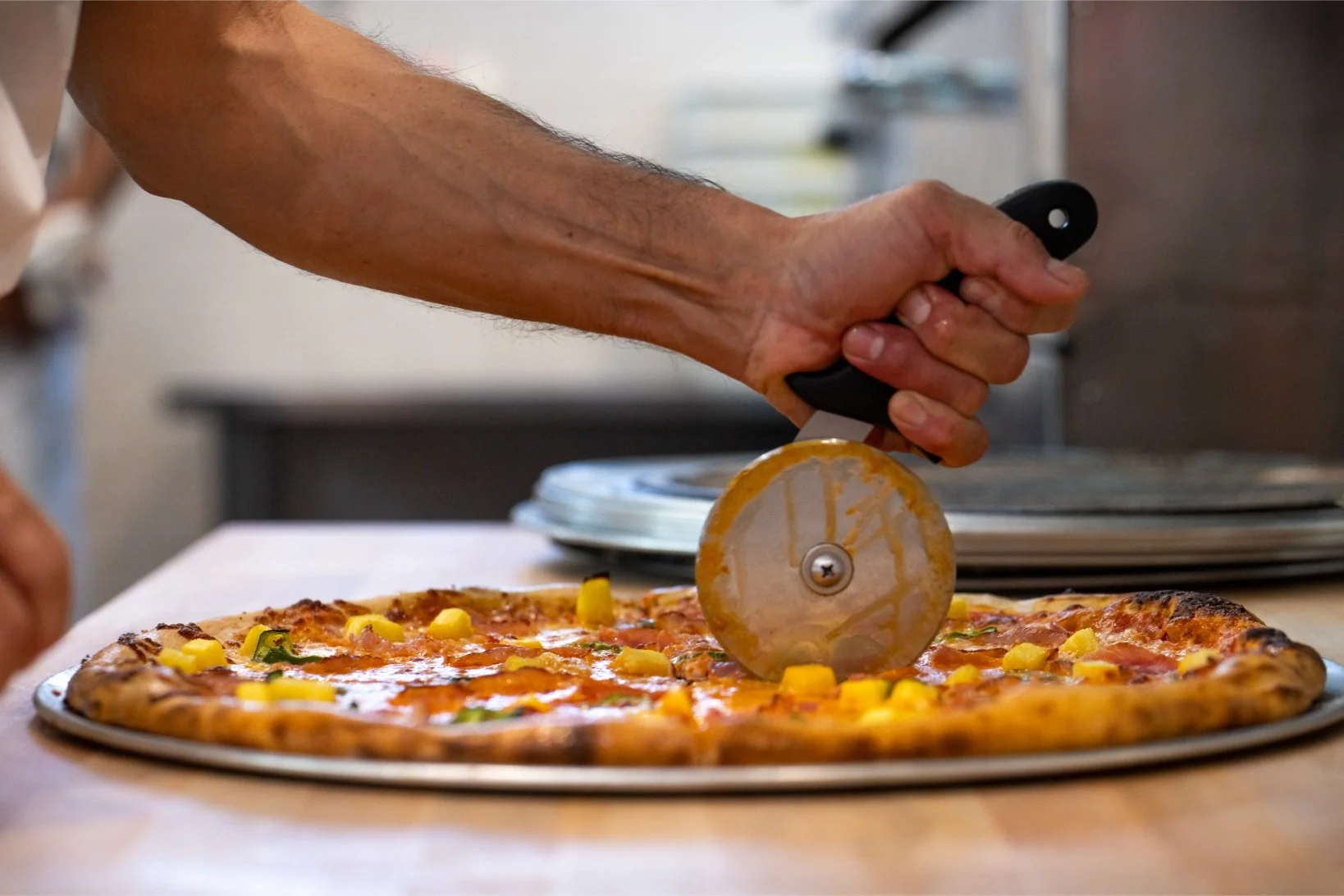 A person slicing a pizza with a pizza cutter in a kitchen.