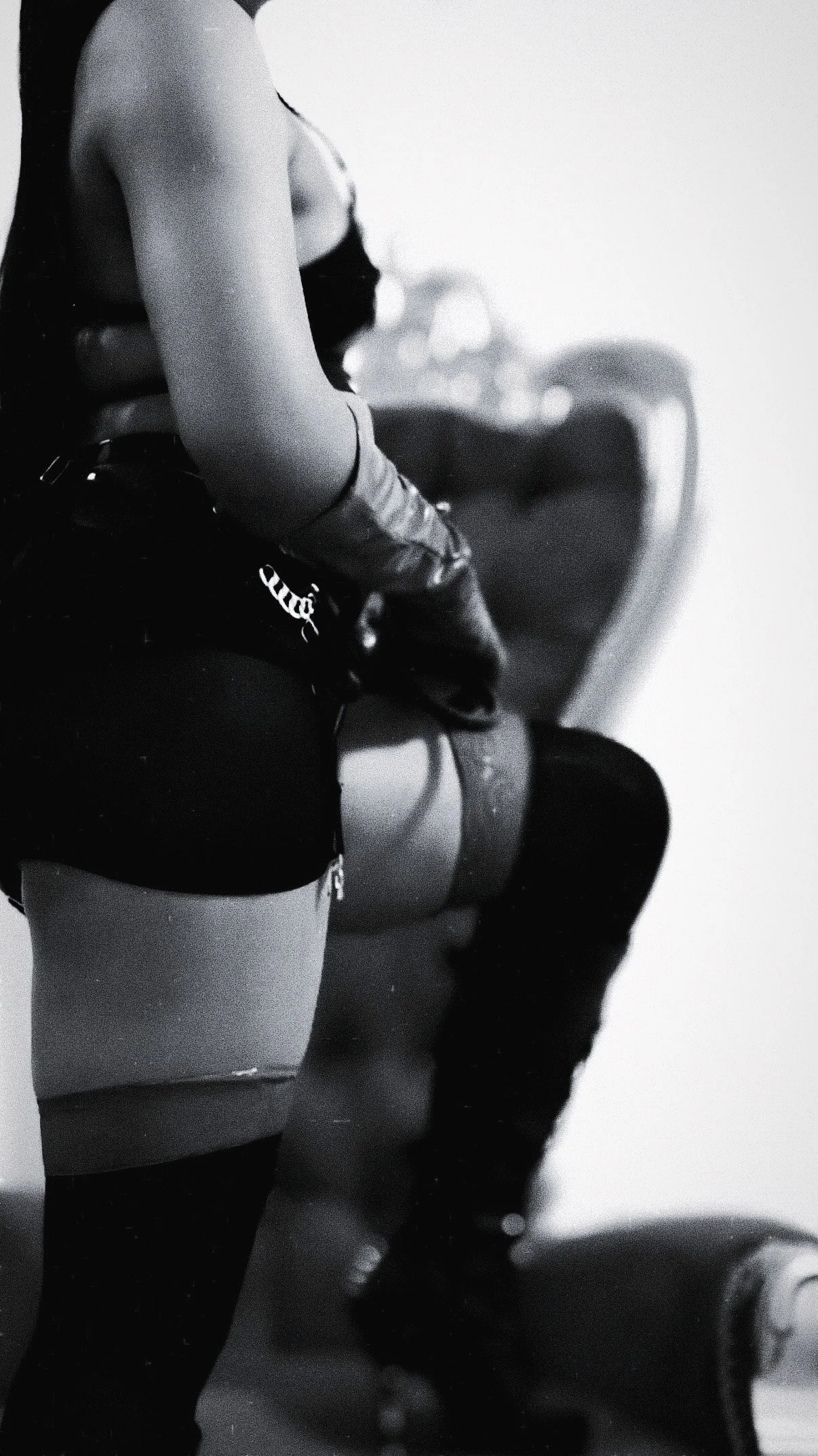 A black-and-white photo of a woman in lingerie and thigh-high stockings sitting on a chair, with her back to the camera.