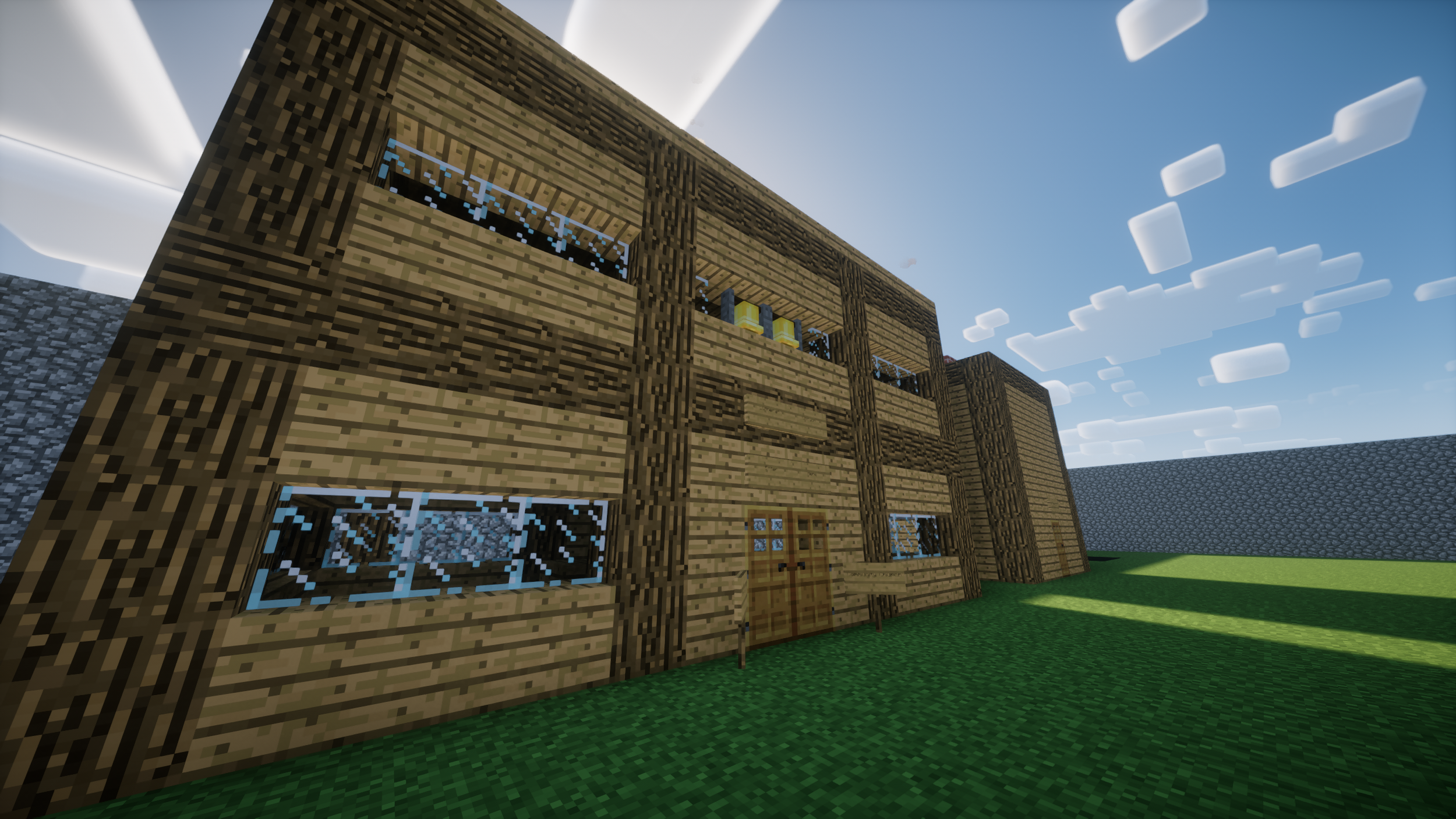 A Minecraft-style wooden house with multiple windows, a door, and a staircase on a grassy area under a blue sky with clouds.
