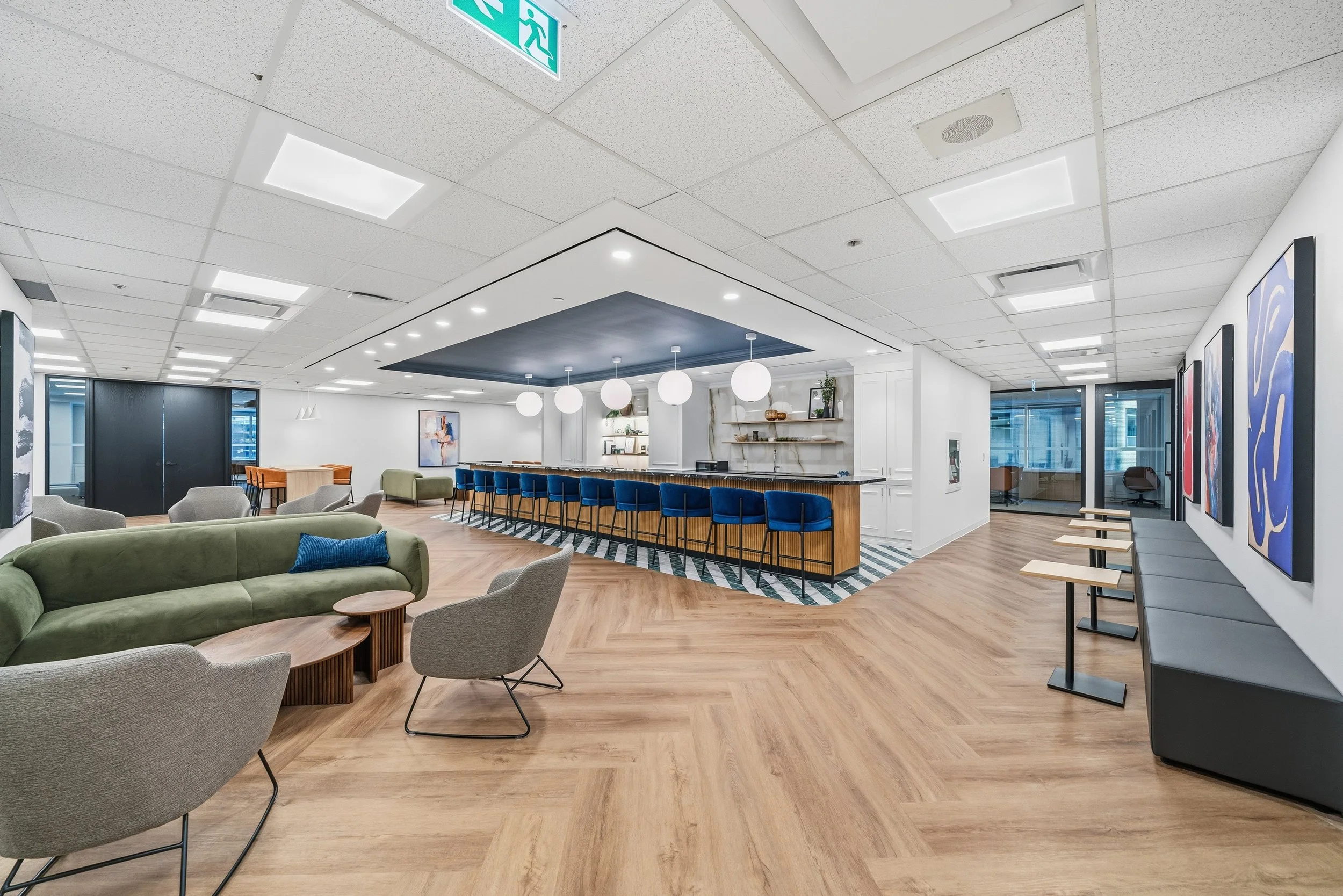 Modern hotel lounge with seating area, bar with blue chairs, artwork on the walls, and large windows letting in natural light.