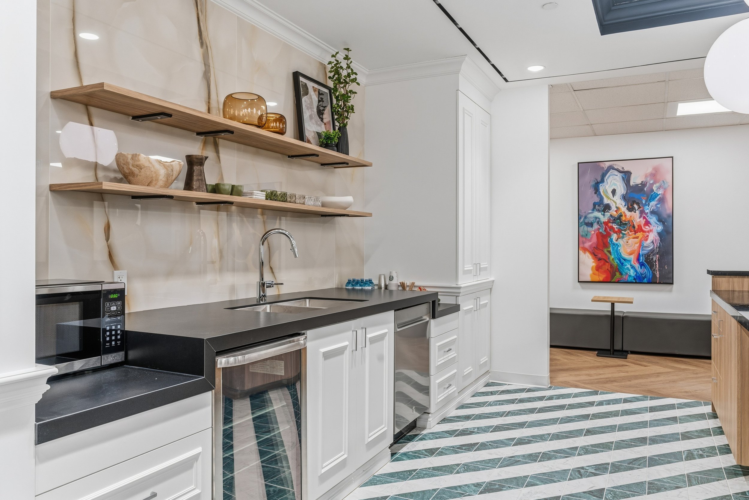 Modern kitchen with black countertops, white cabinets, two wooden open shelves with decorative items, and a colorful abstract painting on the wall.