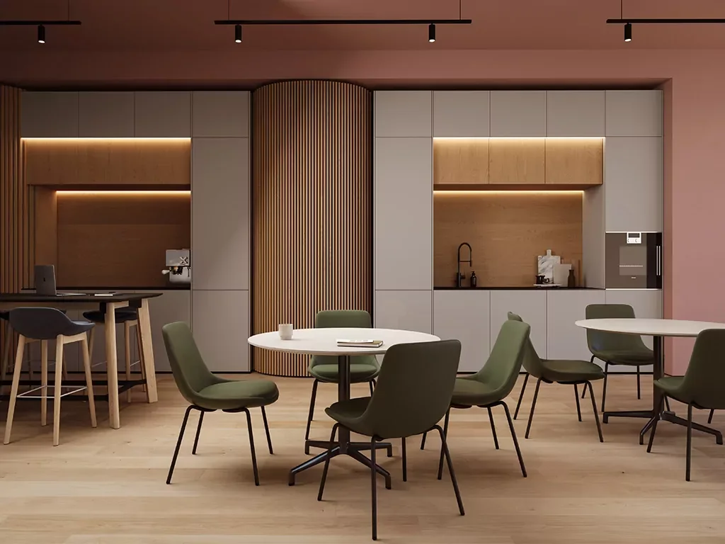 Modern kitchen with gray cabinets, wooden accents, and a small coffee area, adjacent to a dining space with round tables and green chairs.