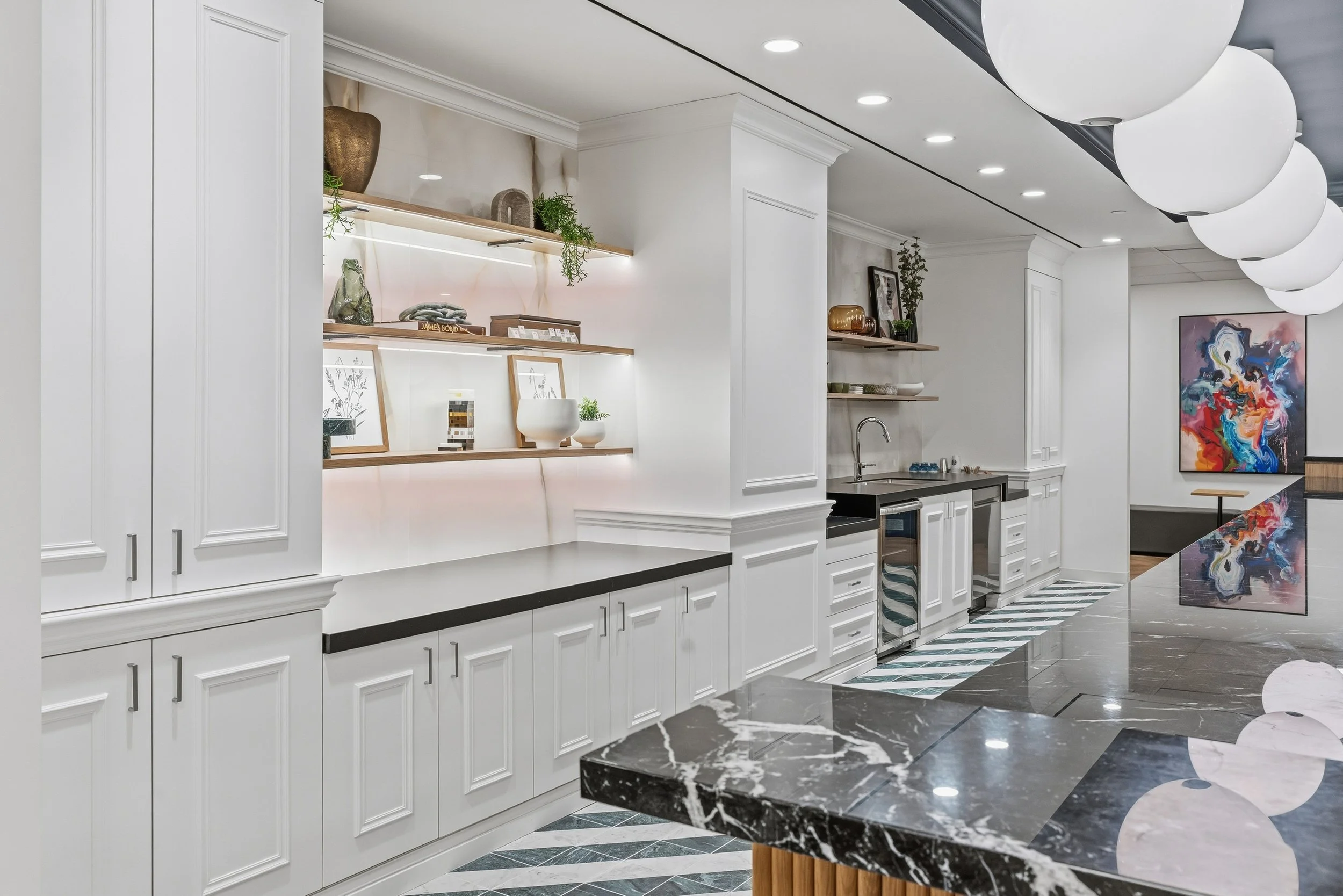Modern kitchen with white cabinets, black countertops, and open shelves displaying decorative items. There is a black marble island with white veining and a colorful abstract painting on the wall.