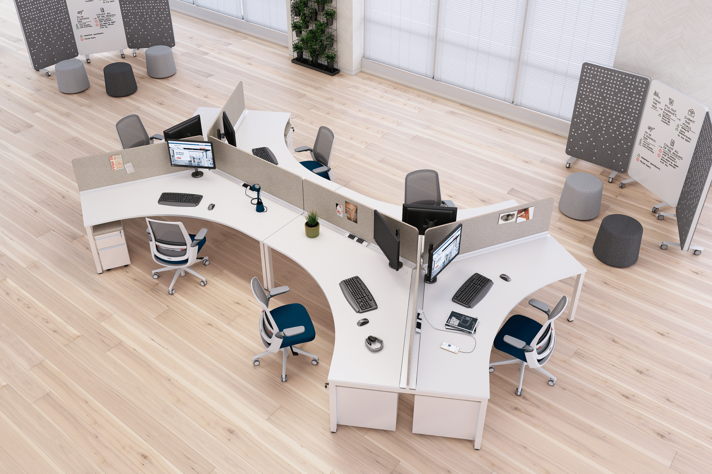 Open-concept modern office space with multiple workstations, ergonomic chairs, computer monitors, and white desks arranged in a curve. There are two whiteboards with diagrams and notes on stands, and a tall plant near the window with blinds. The light wood flooring adds warmth to the room.