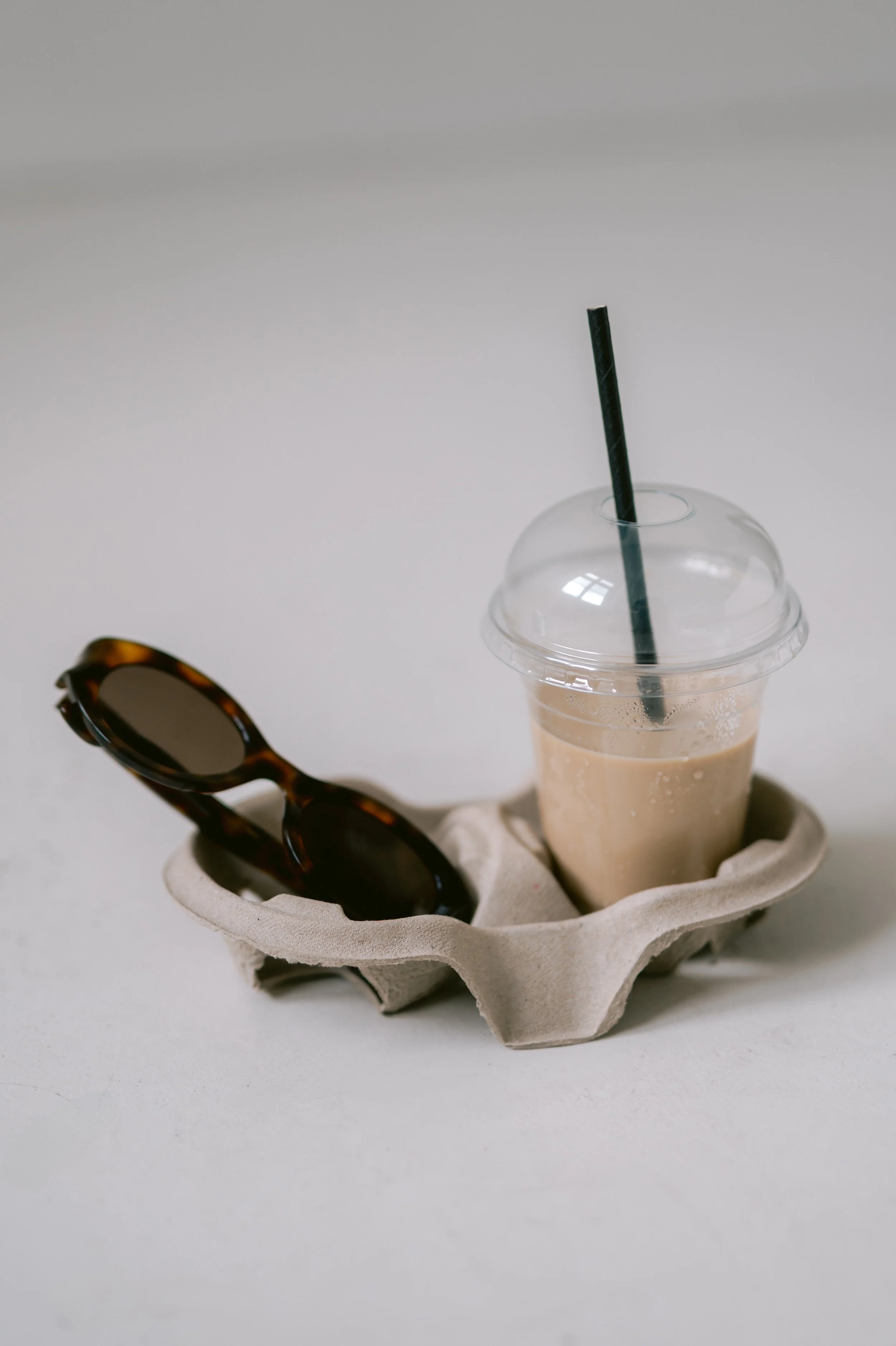 An egg carton tray holding sunglasses and a plastic cup with iced coffee and a straw.