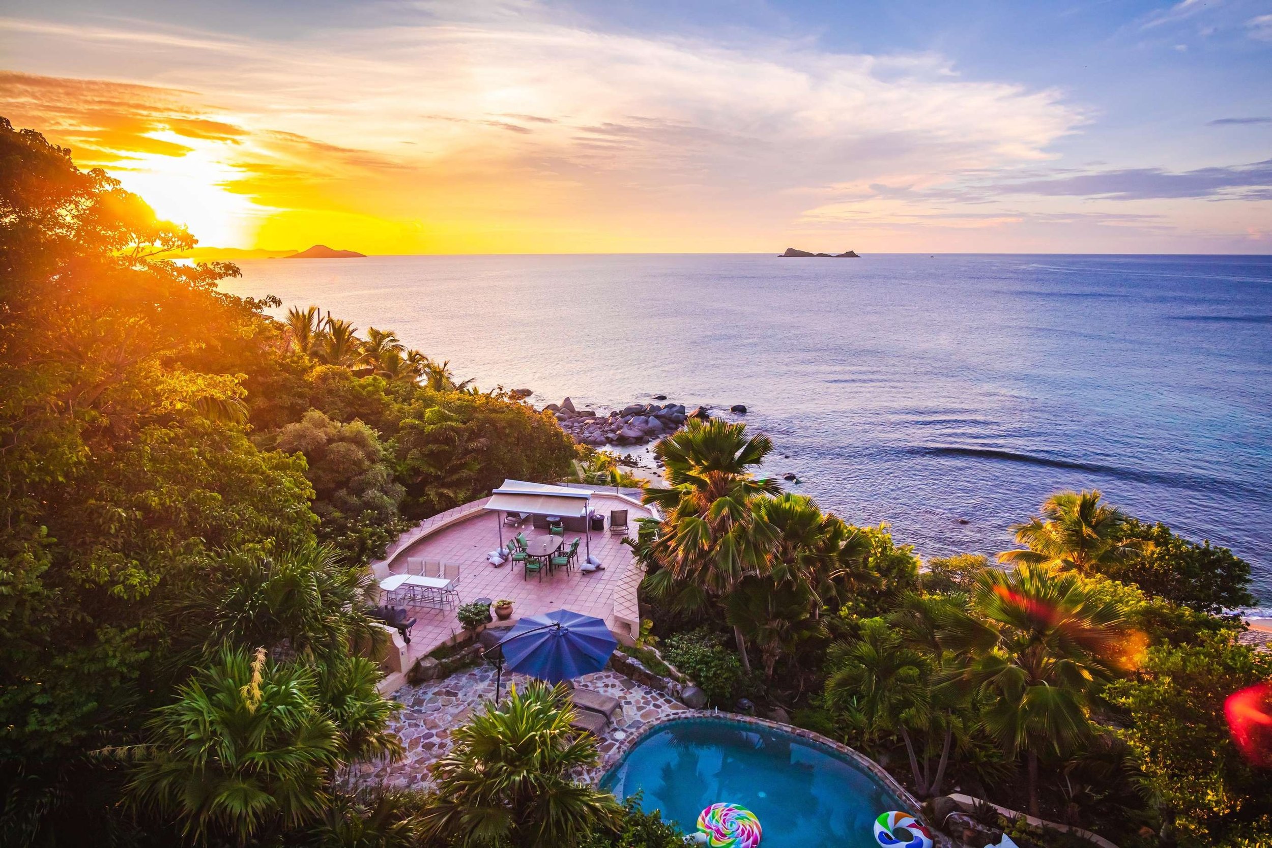Sunset view over the ocean with a lush, tropical garden and swimming pool in the foreground.