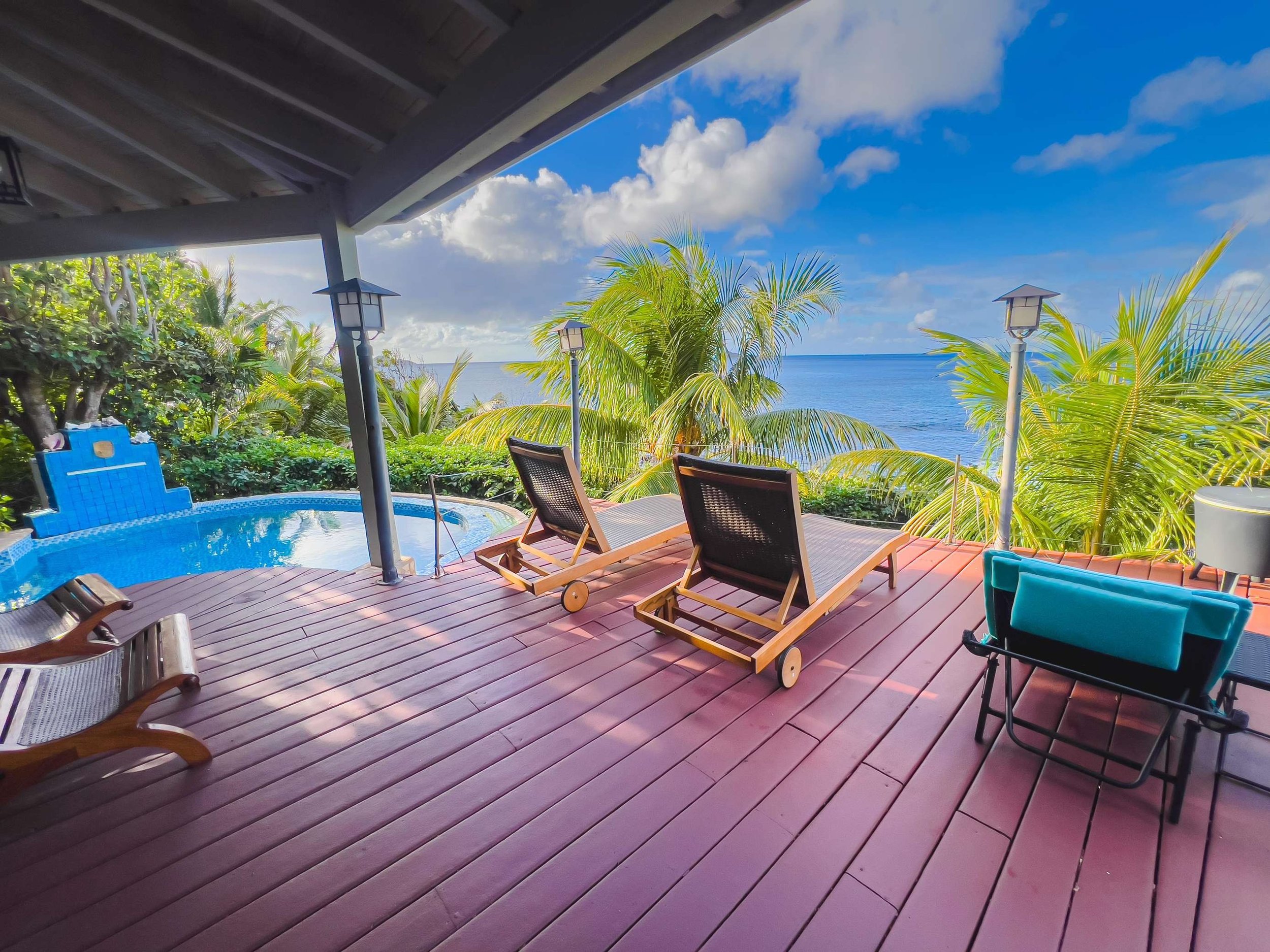 A patio with two lounge chairs, a small hot tub, and tropical plants overlooking the ocean on a sunny day.