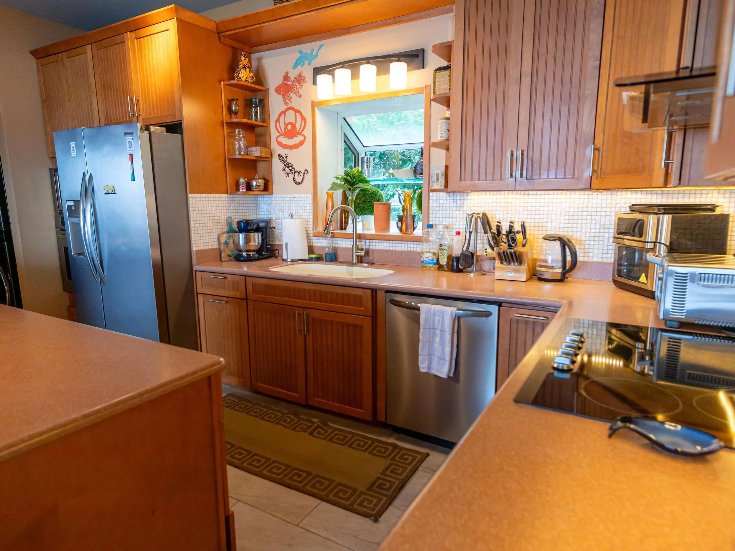 A kitchen with wooden cabinets, stainless steel appliances, a window with plants outside, and various kitchen utensils on the countertops.