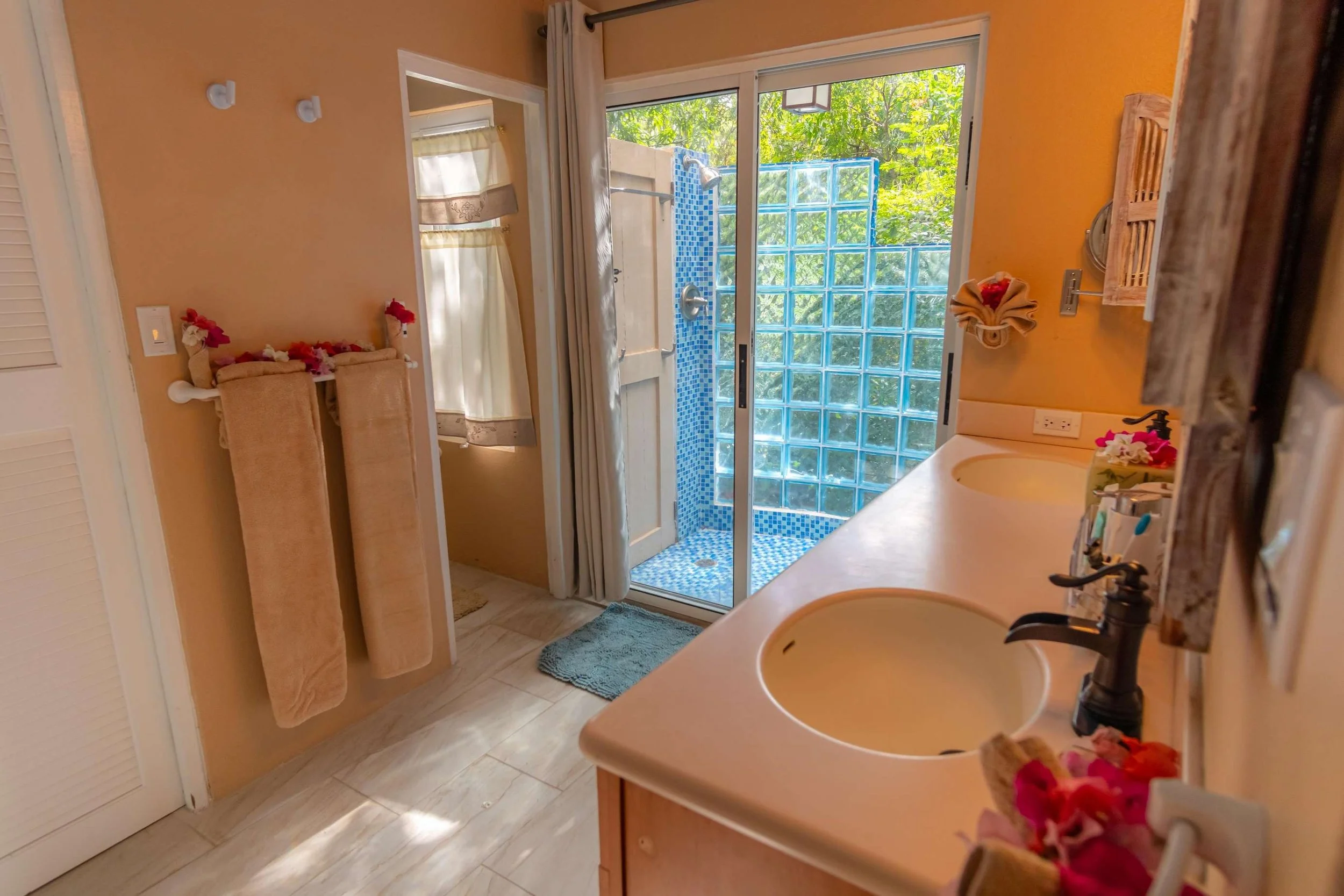 Bathroom with dual sinks, a glass-block shower, and a small outdoor shower area through glass sliding doors.