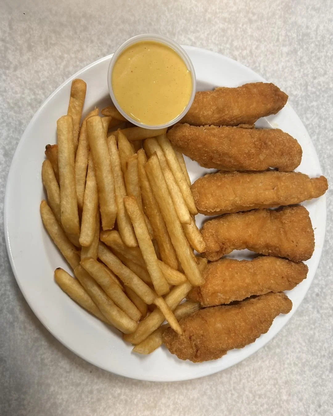 Plate with French fries, chicken tenders, and dipping sauce on top.