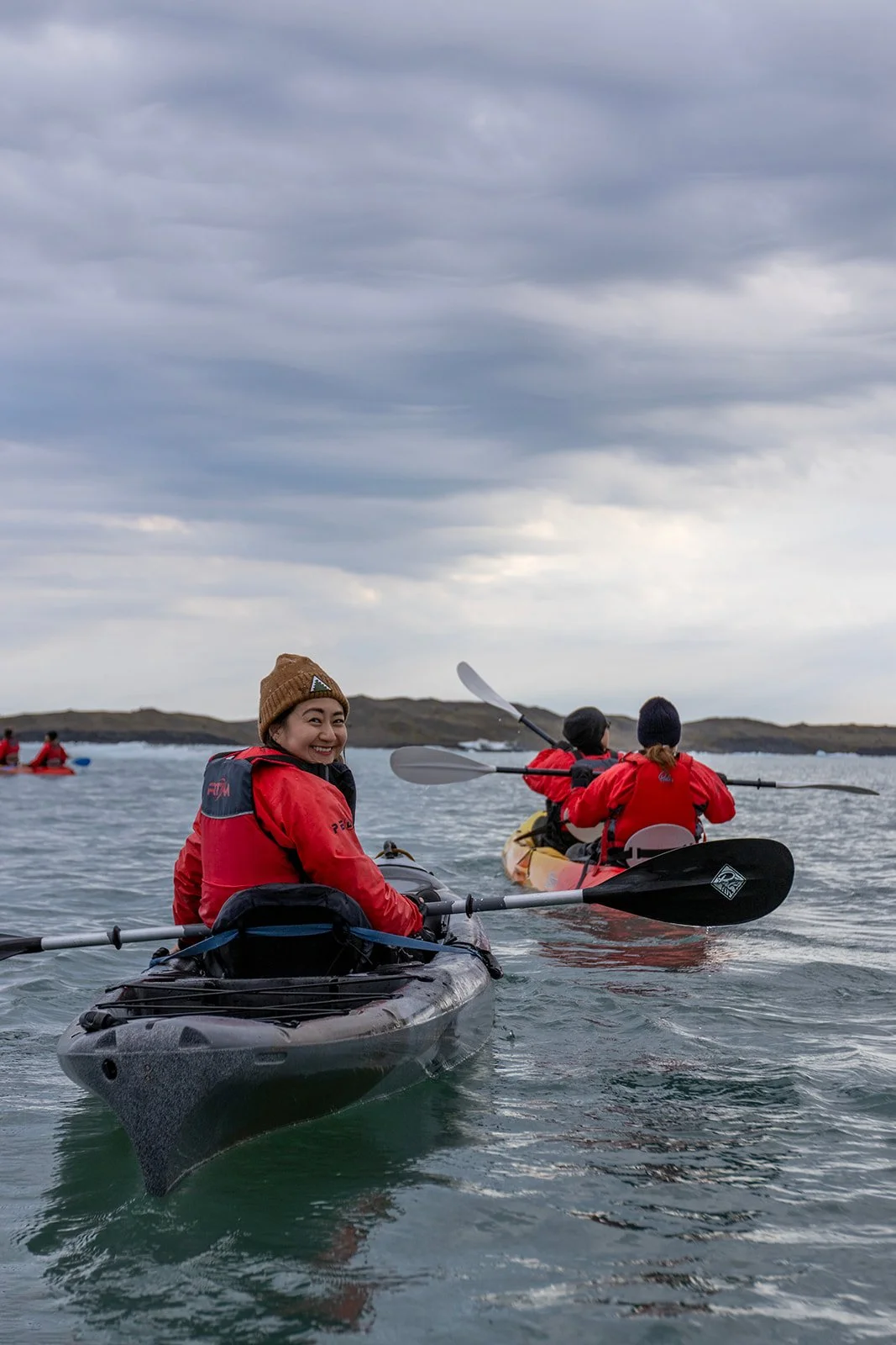 Group of people kayaking on the water during cloudy weather, with a woman smiling and looking at the camera.