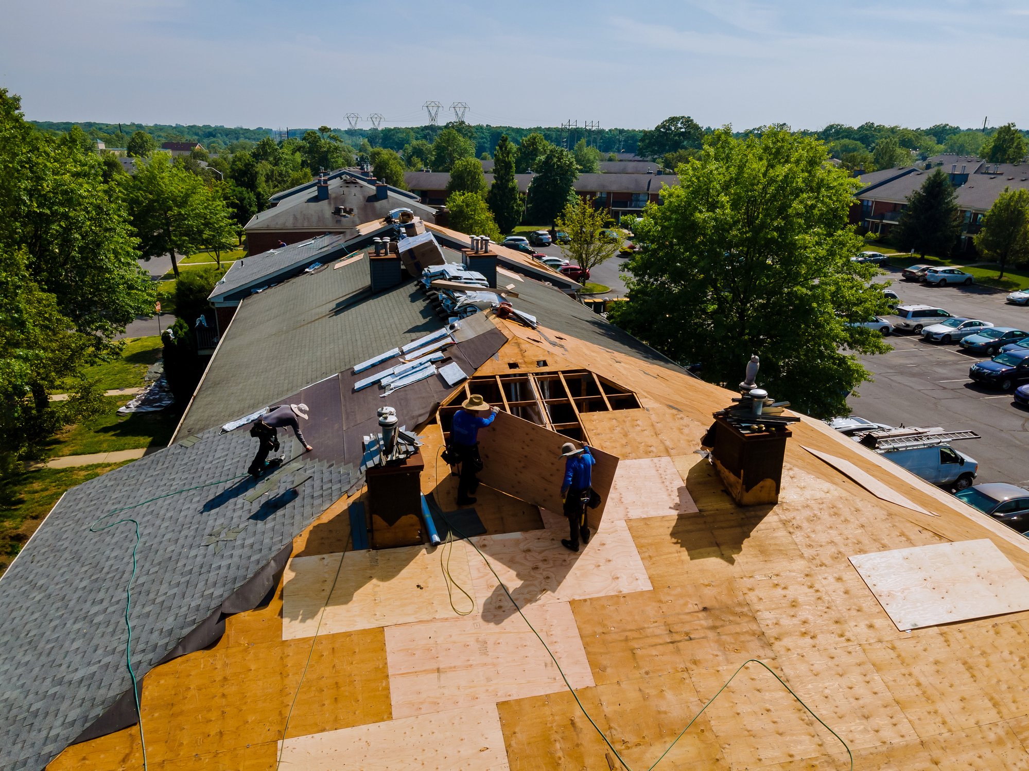 Construction workers repairing or replacing the roof of a building in a residential area during the daytime.