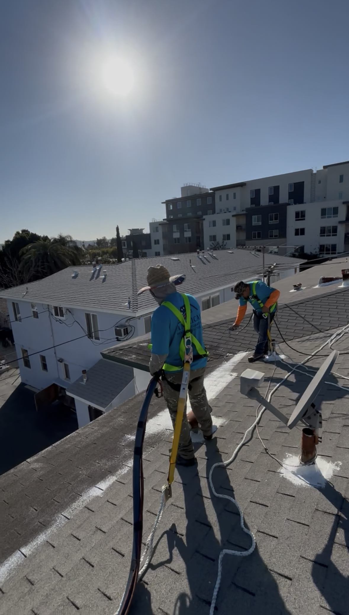 Workers repairing a rooftop under a clear blue sky with the sun shining brightly.