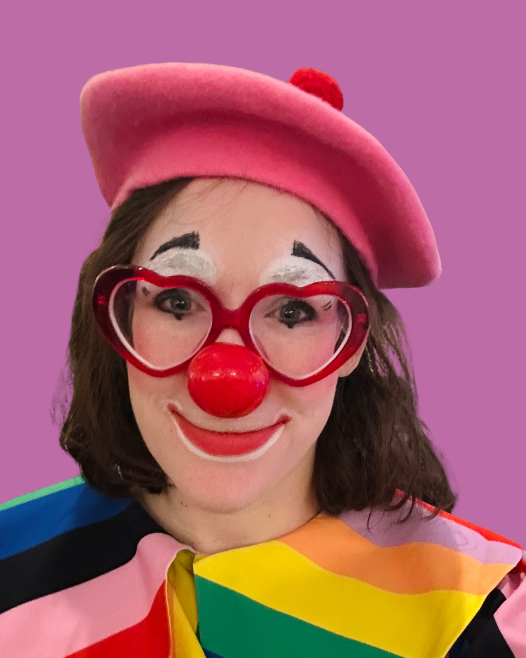 a clown with a pink beret hat, red heart glasses, a red nose, and a rainbow top