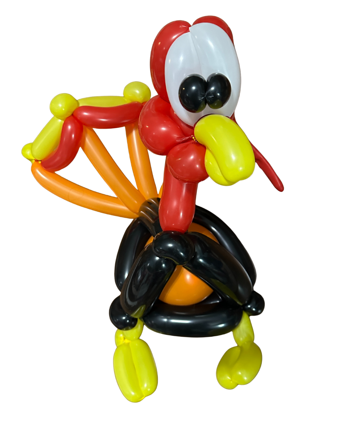 Colorful balloon sculpture of a turkey with large black and white eyes, a yellow beak, and red, yellow, black, and orange balloons forming the body, limbs and feathers.