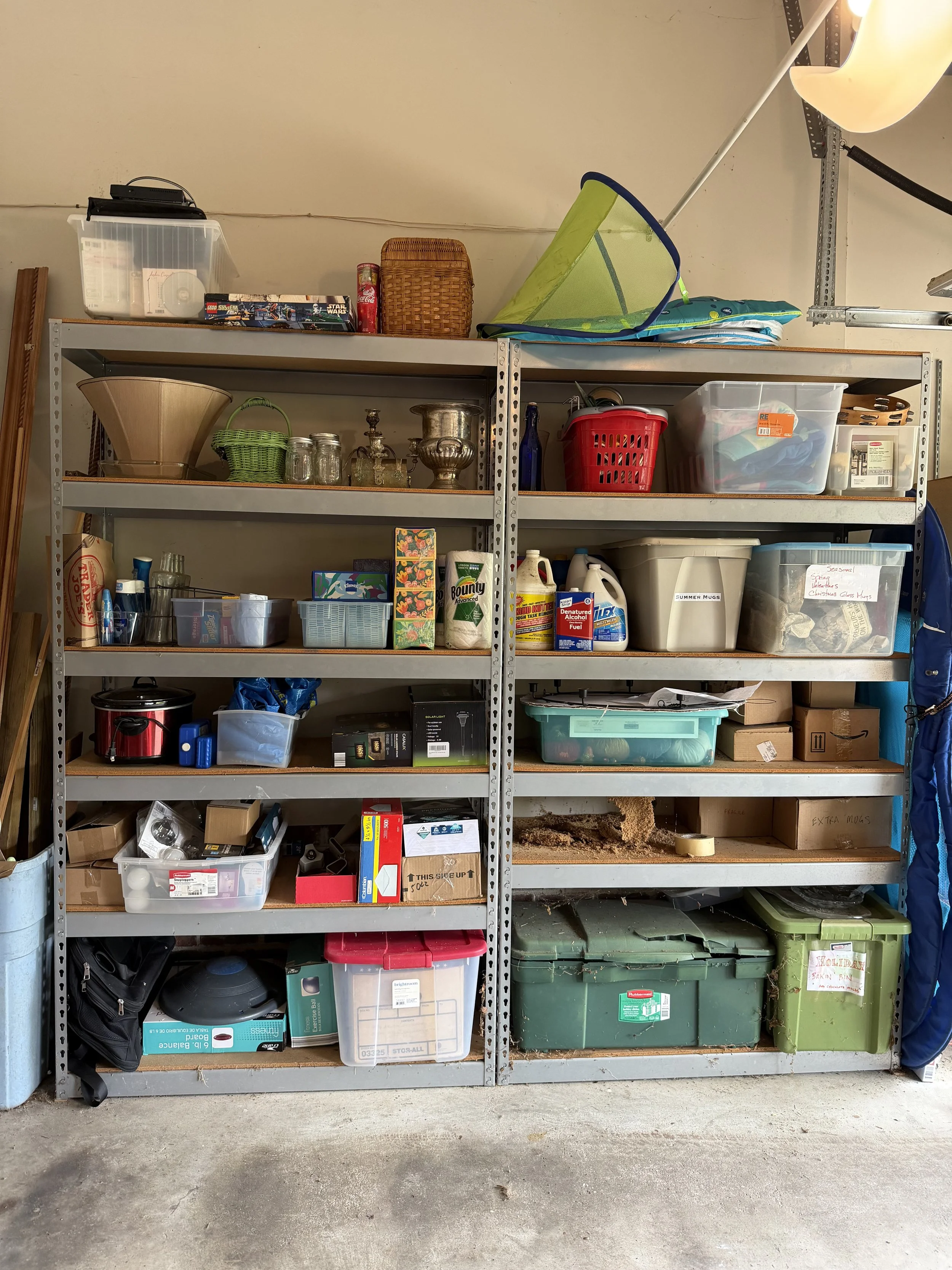 Metal shelving unit filled with various household items, tools, storage containers, and miscellaneous objects, located in a garage.