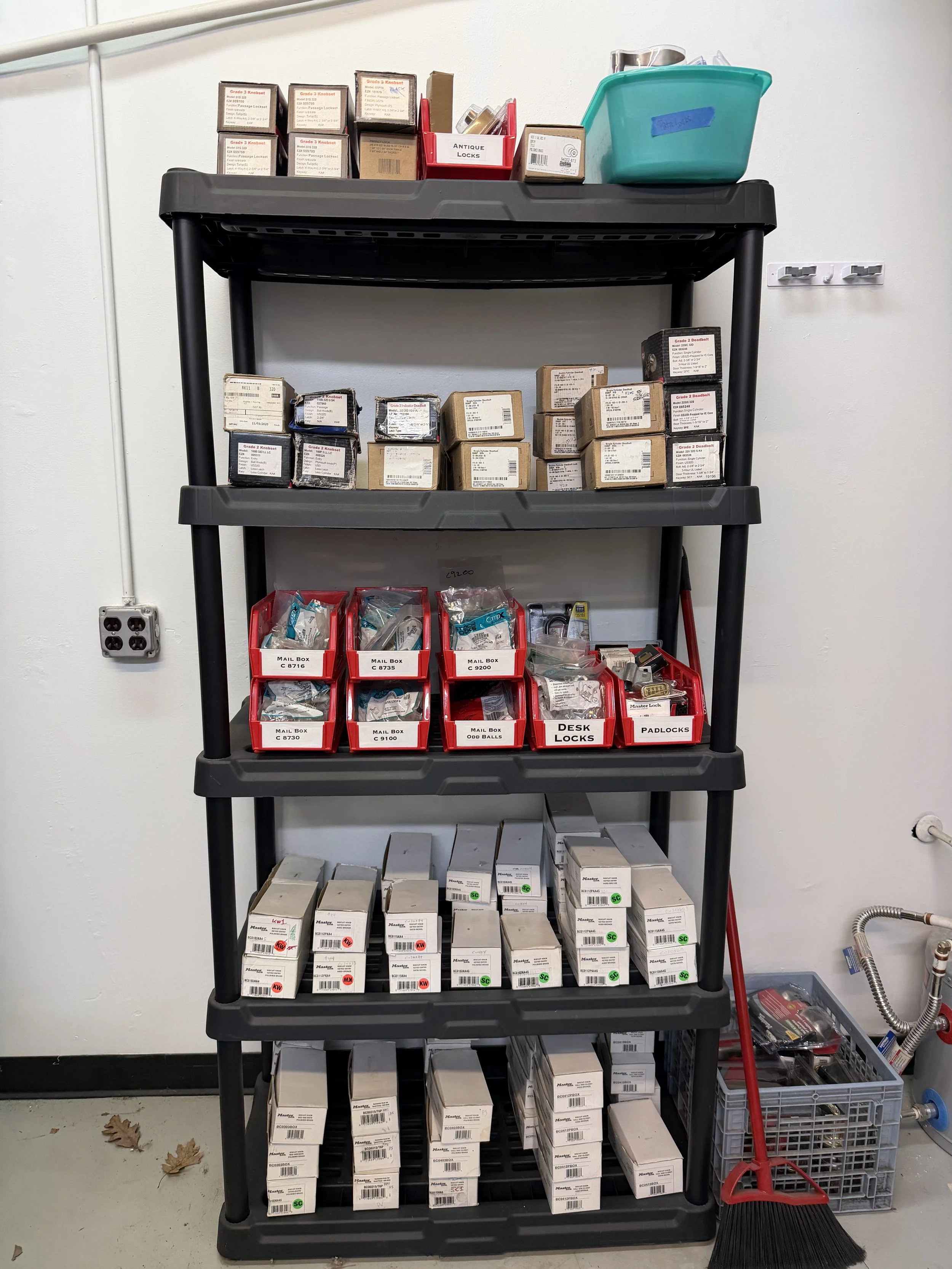 A black storage rack filled with various hardware items, including boxes of locks, keys, and hardware accessories, in a workshop or storage room for commercial organization.