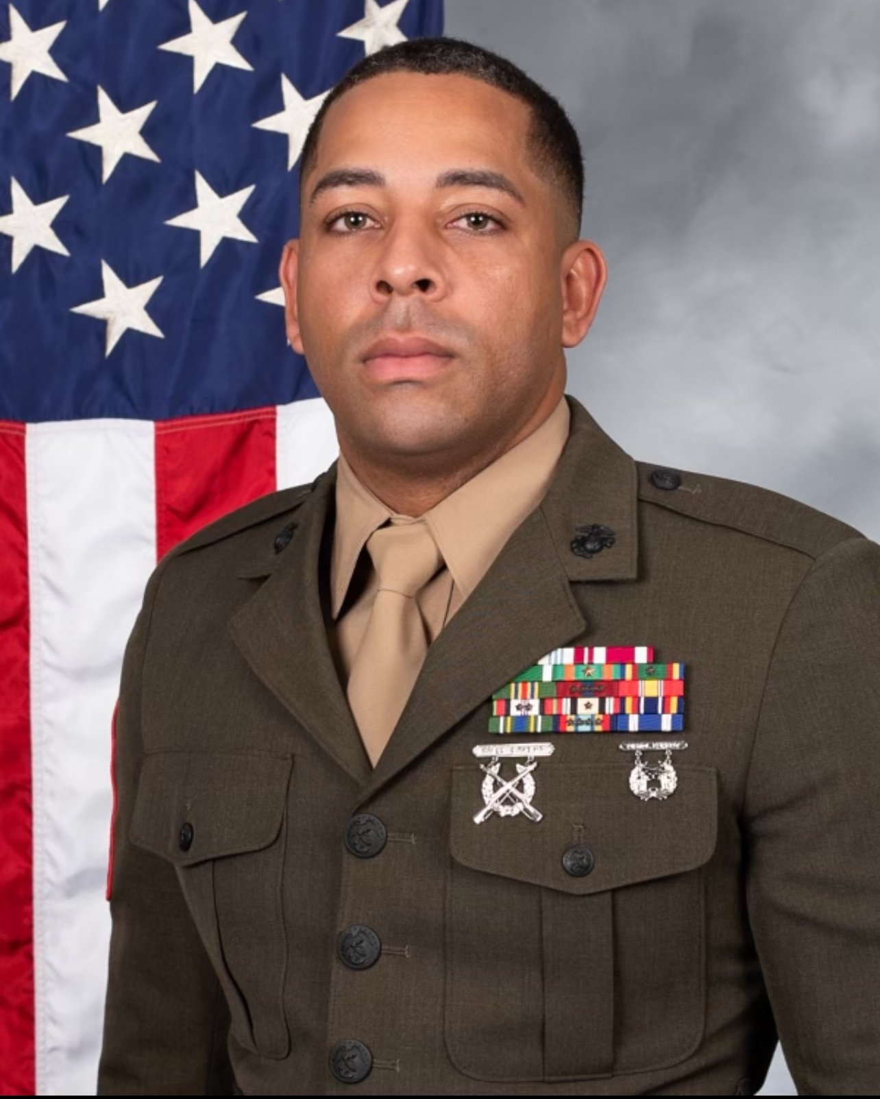 A man in a military uniform standing in front of an American flag.