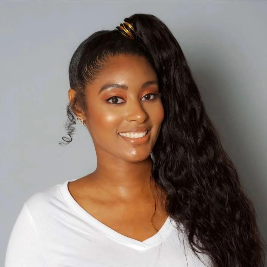 Portrait of a smiling woman with long wavy hair, wearing a white top, against a plain gray background.