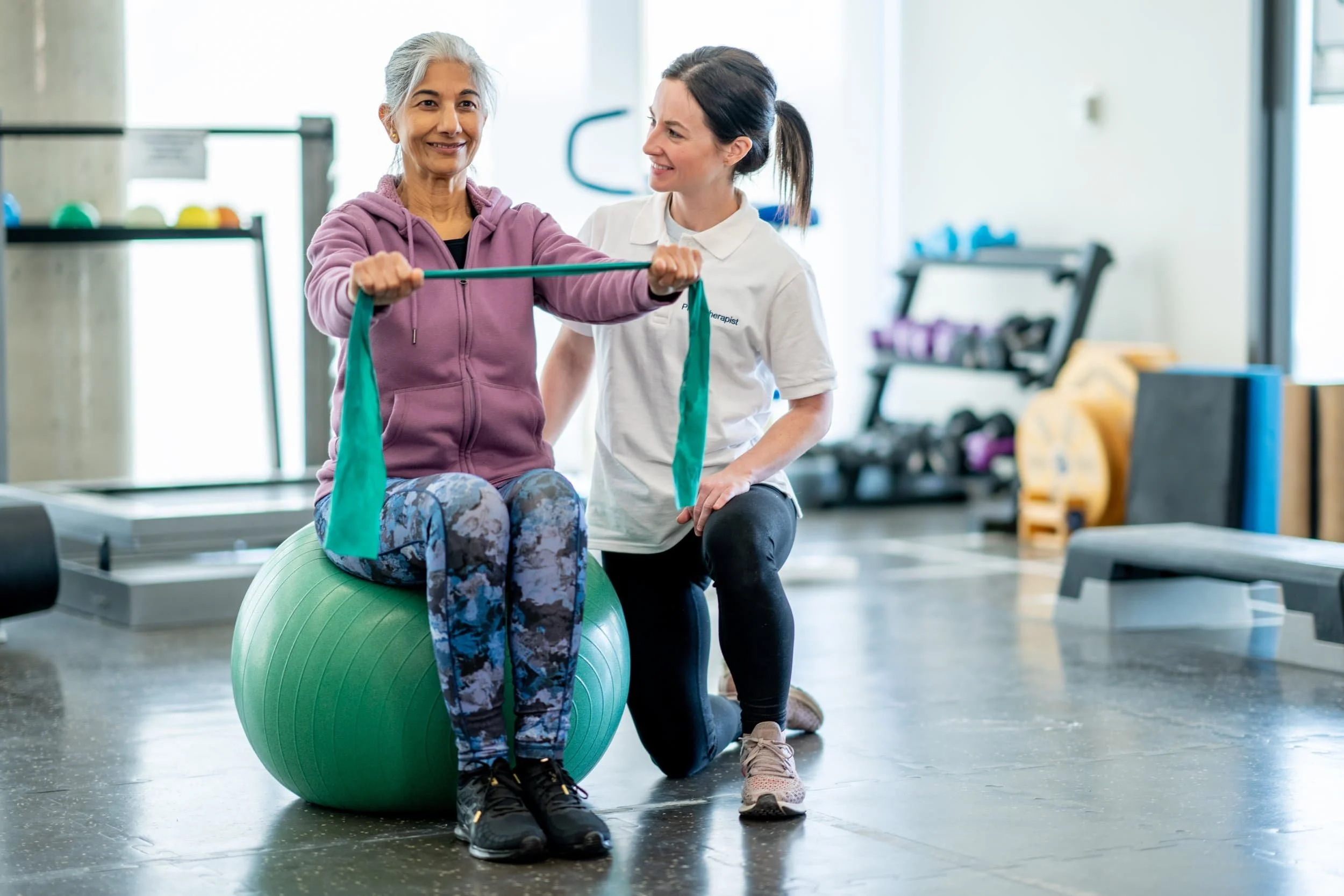 Elderly woman balancing on a medicine ball while receiving physical therapy
