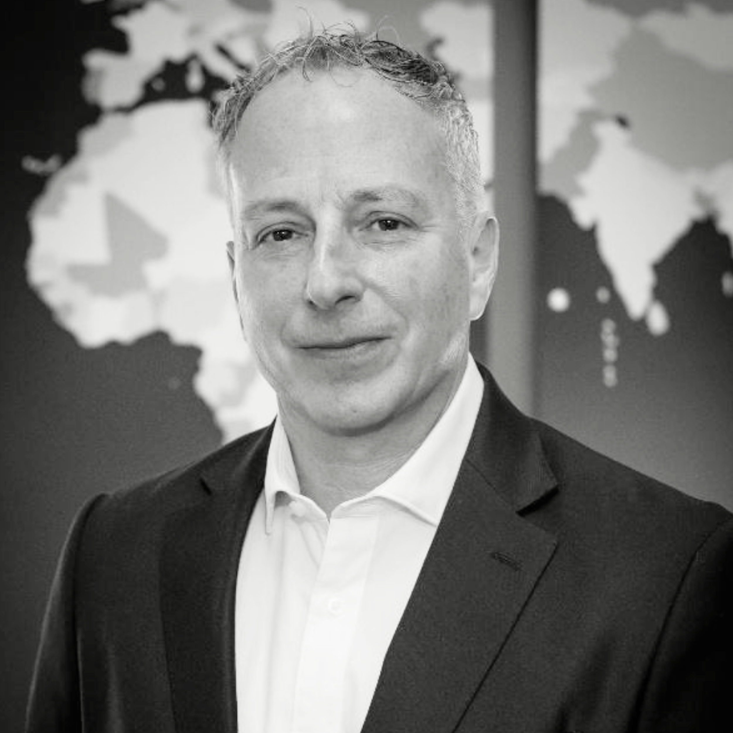 Black and white portrait of a man in a suit with a world map in the background.