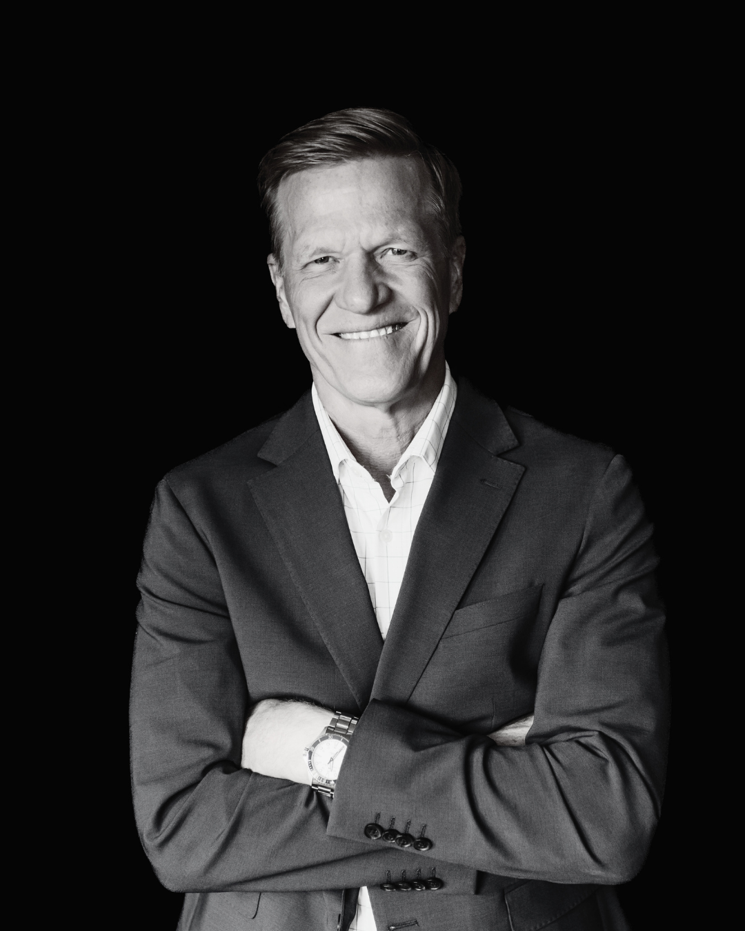 Black and white photo of a smiling man with short, light-colored hair, wearing a dark shirt.