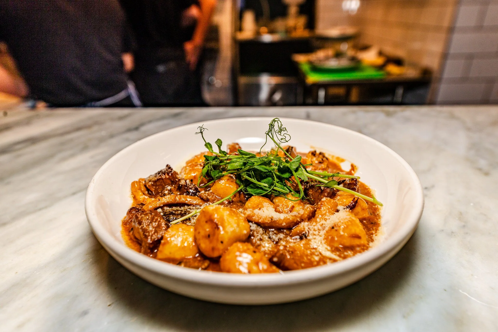 A bowl of gnocchi with sauce, garnished with microgreens on a marble countertop in a restaurant setting.