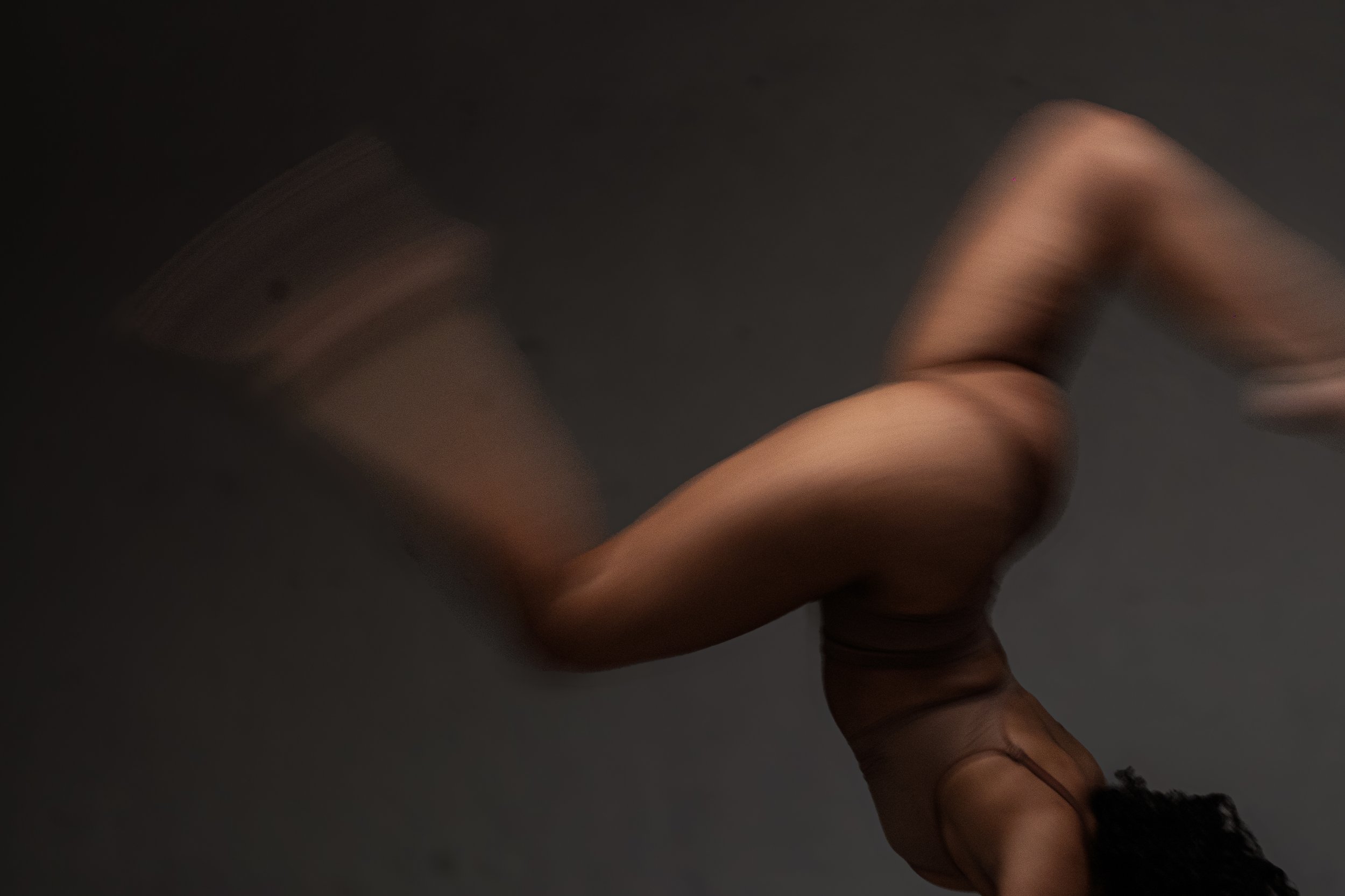 A person's hand with dark skin is seen against a dark background. The hand is partially curled, with fingers slightly bent, and appears to be in motion or gesture.