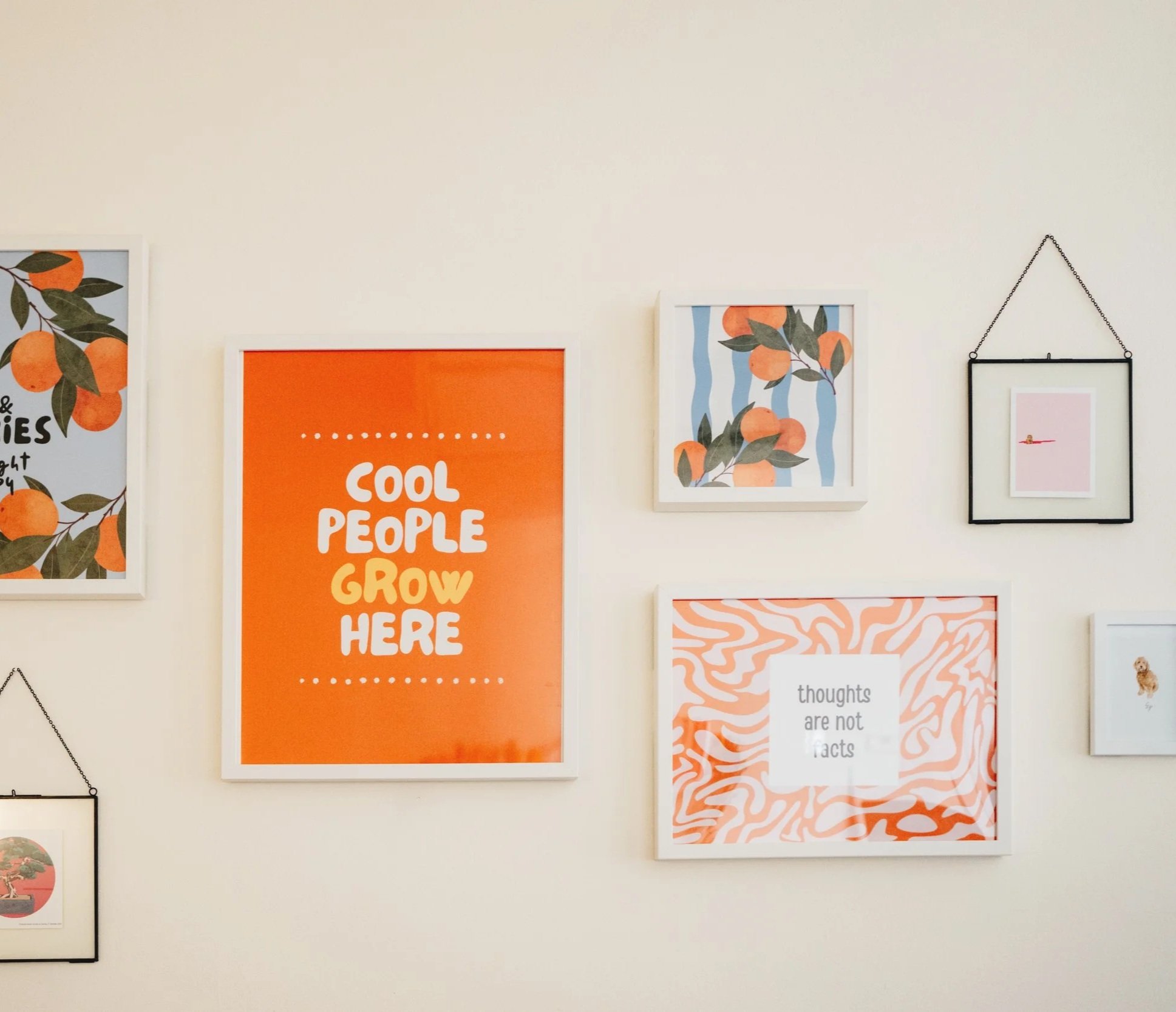 Gallery wall with colorful framed prints, including one with orange text that says "Cool People Grow Here" and another with orange and white abstract pattern with text "thoughts are not facts."