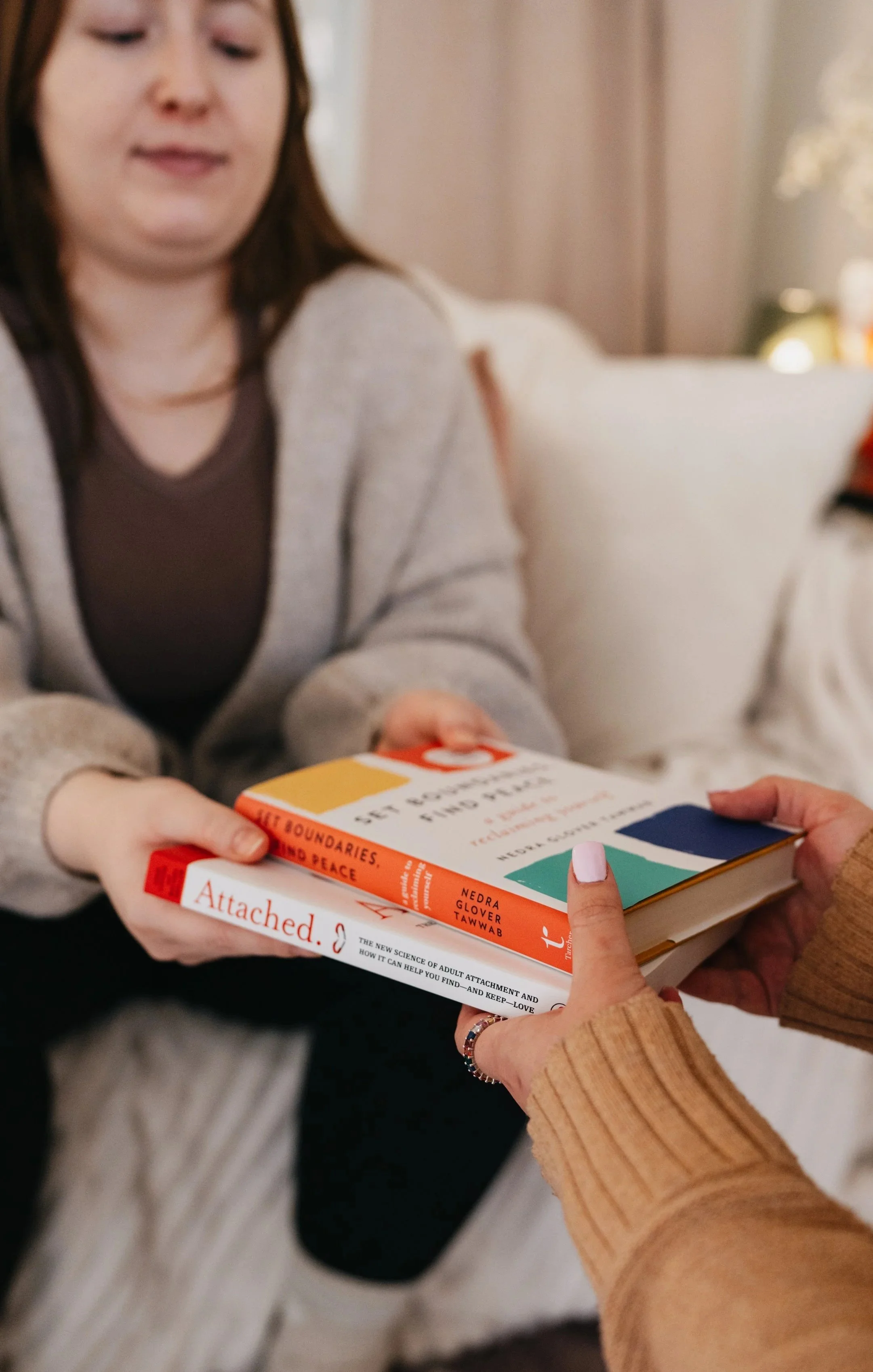 A woman receives a book titled 'Set Boundaries, Find Peace' from another person whose hands are visible, in a cozy indoor setting.