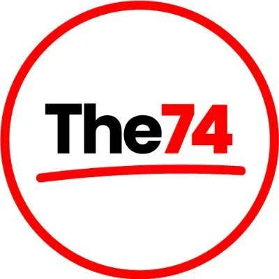 The logo of The 74, featuring black and red text inside a red circle.
